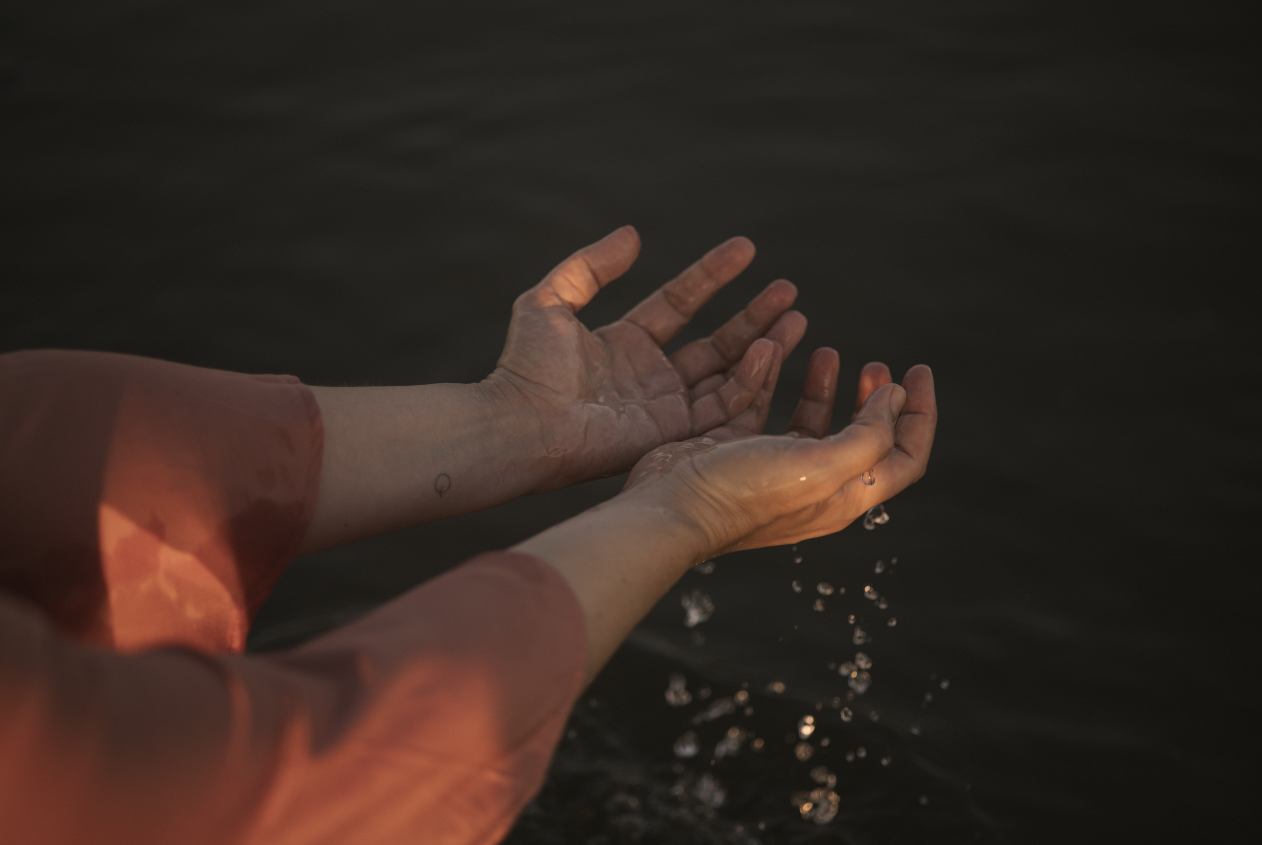 Hände, die Wasser in einer dunklen Wasserquelle aufnehmen, bei Sonnenuntergang