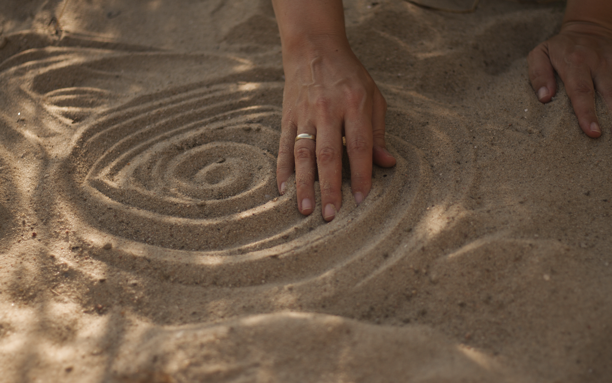 Hand zeichnet ein Auge in den Sand.