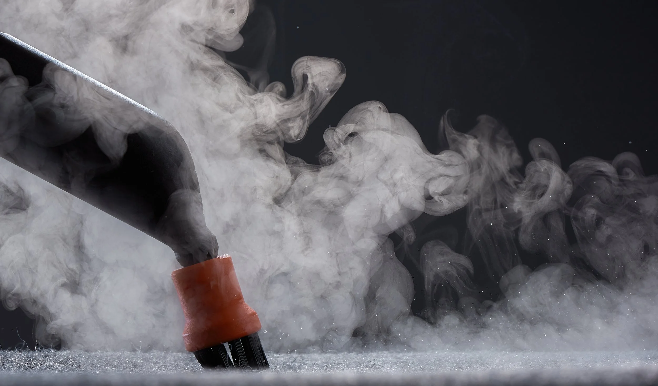 A stick with a red rubber end touching a surface, emitting a cloud of white smoke or vapor against a dark background.