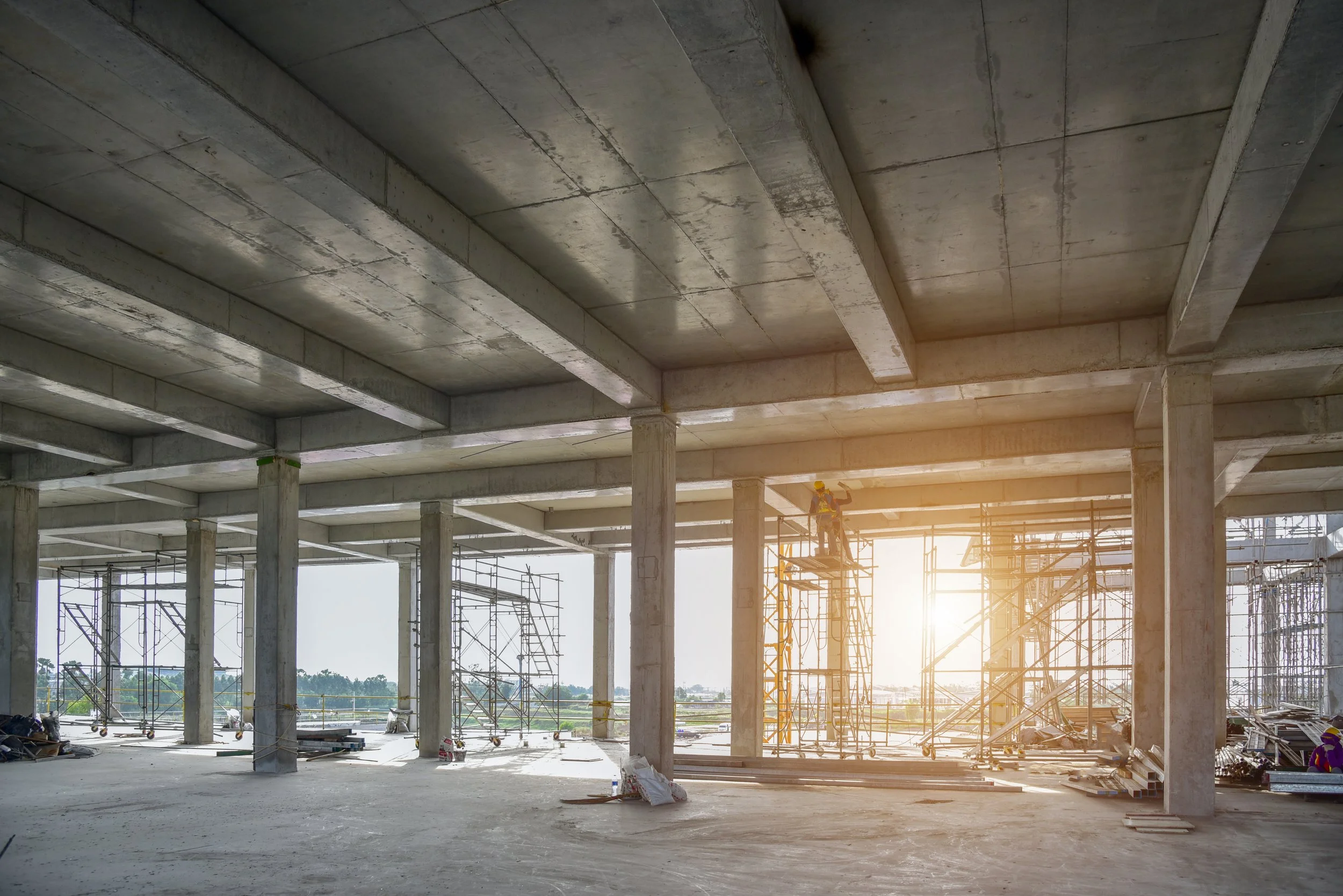 Construction workers on scaffolding inside a large building under construction, with sunlight shining through open spaces in the wall.