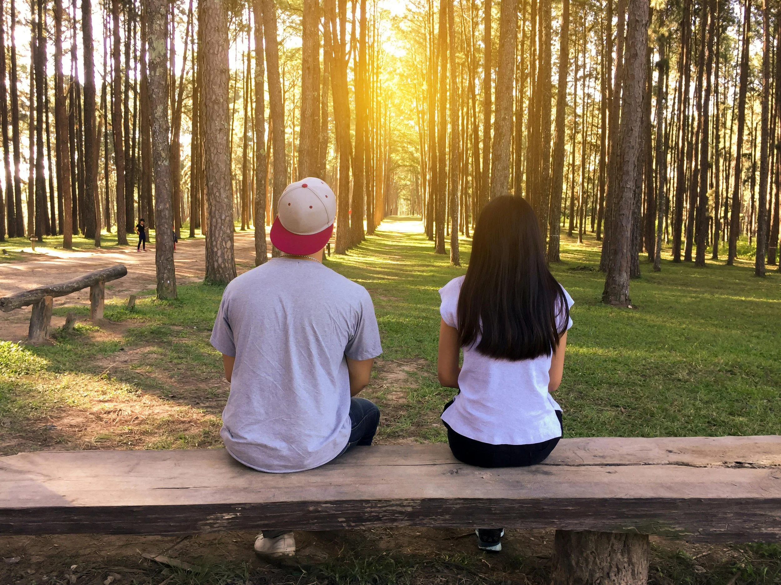 Boy and girl sitting on a bench in a forest at sunset, symbolizing connection, relationships, and healing through guidance and emotional support.