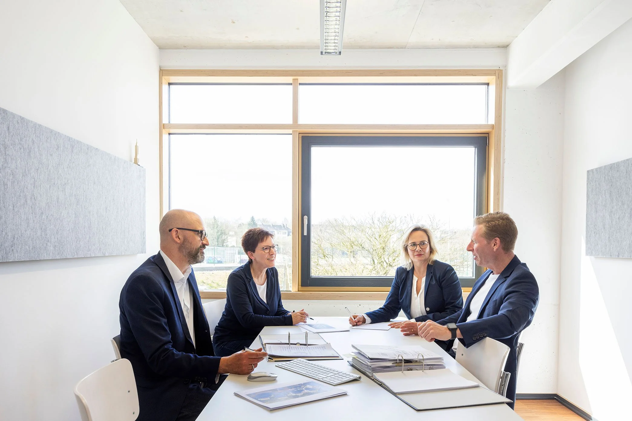 Das kzp Team sitzt an einem Tisch in einem Besprechungsraum und führen ein Gespräch. Der Raum hat große Fenster mit Blick nach draußen und eine helle, minimalistische Einrichtung.