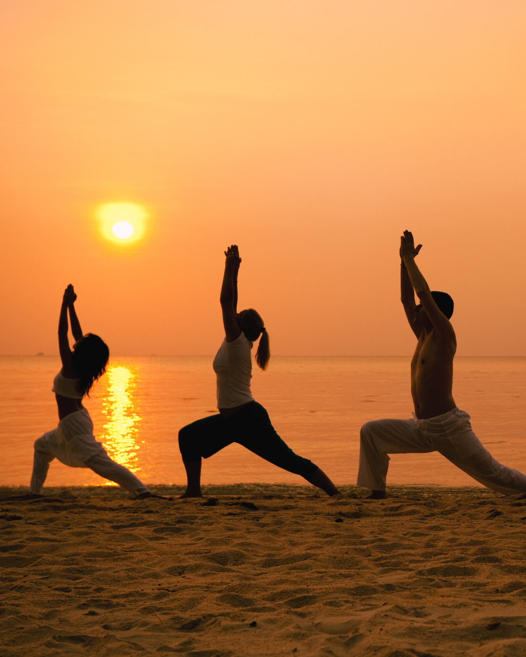 People practicing yoga on the beach during sunset.