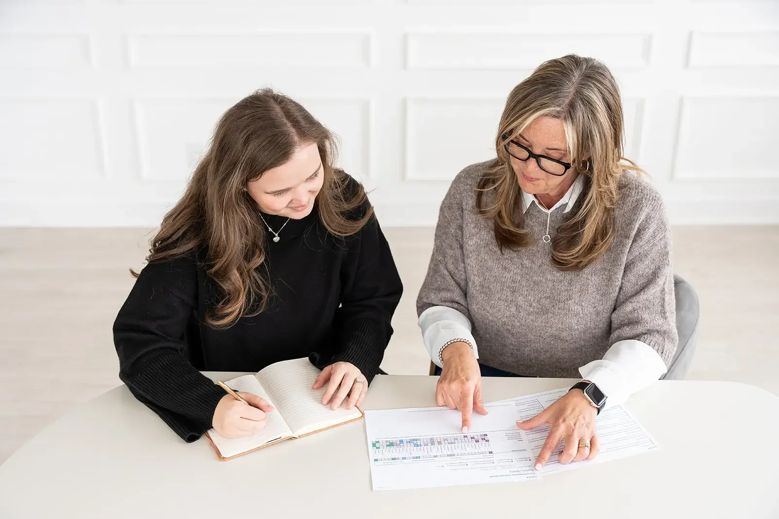 woman writing in journal as consultant reviews data with her.