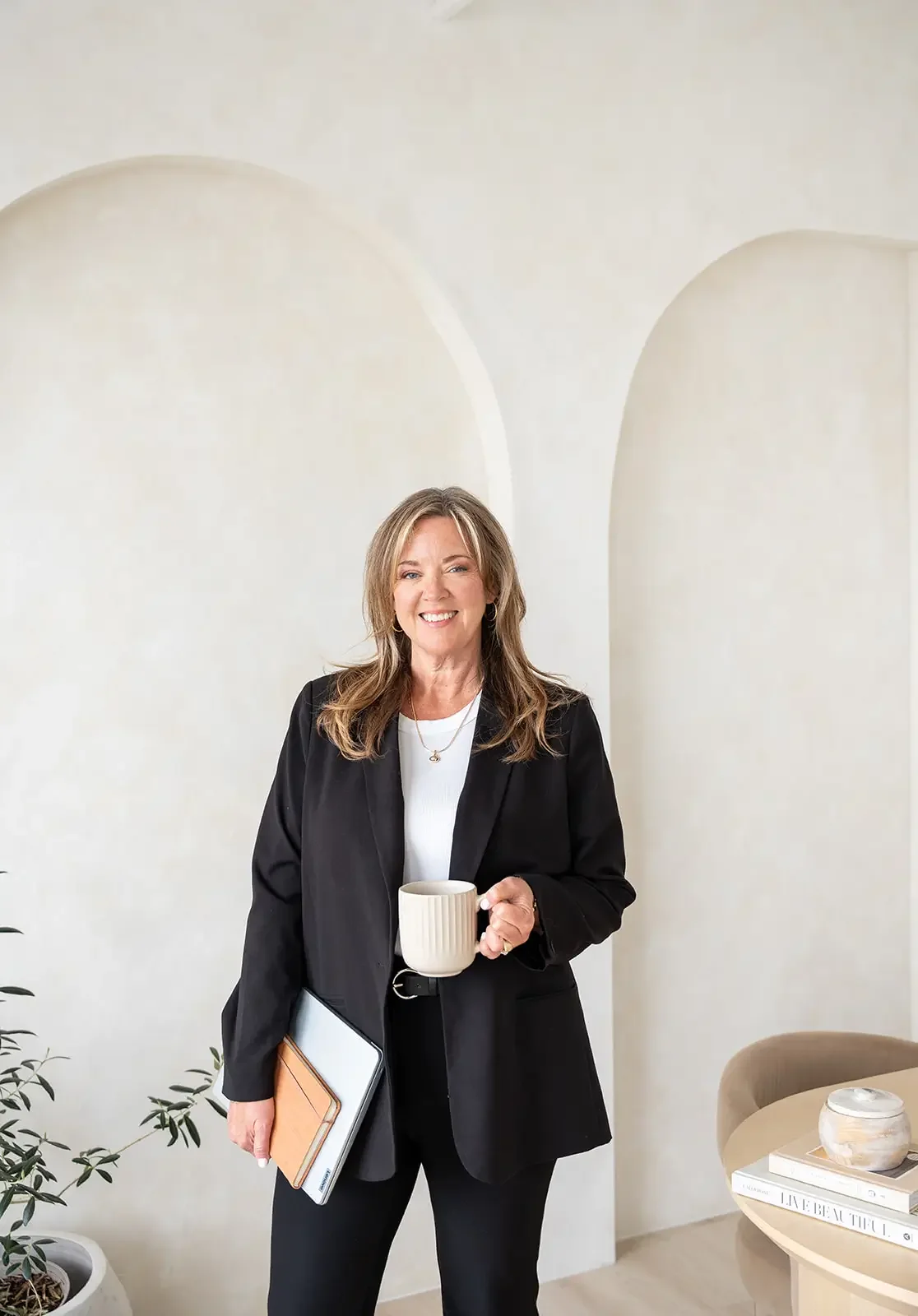 A person working at a desk with a laptop, pointing at a detailed color-coded chart on paper, with a rose gold notebook nearby.