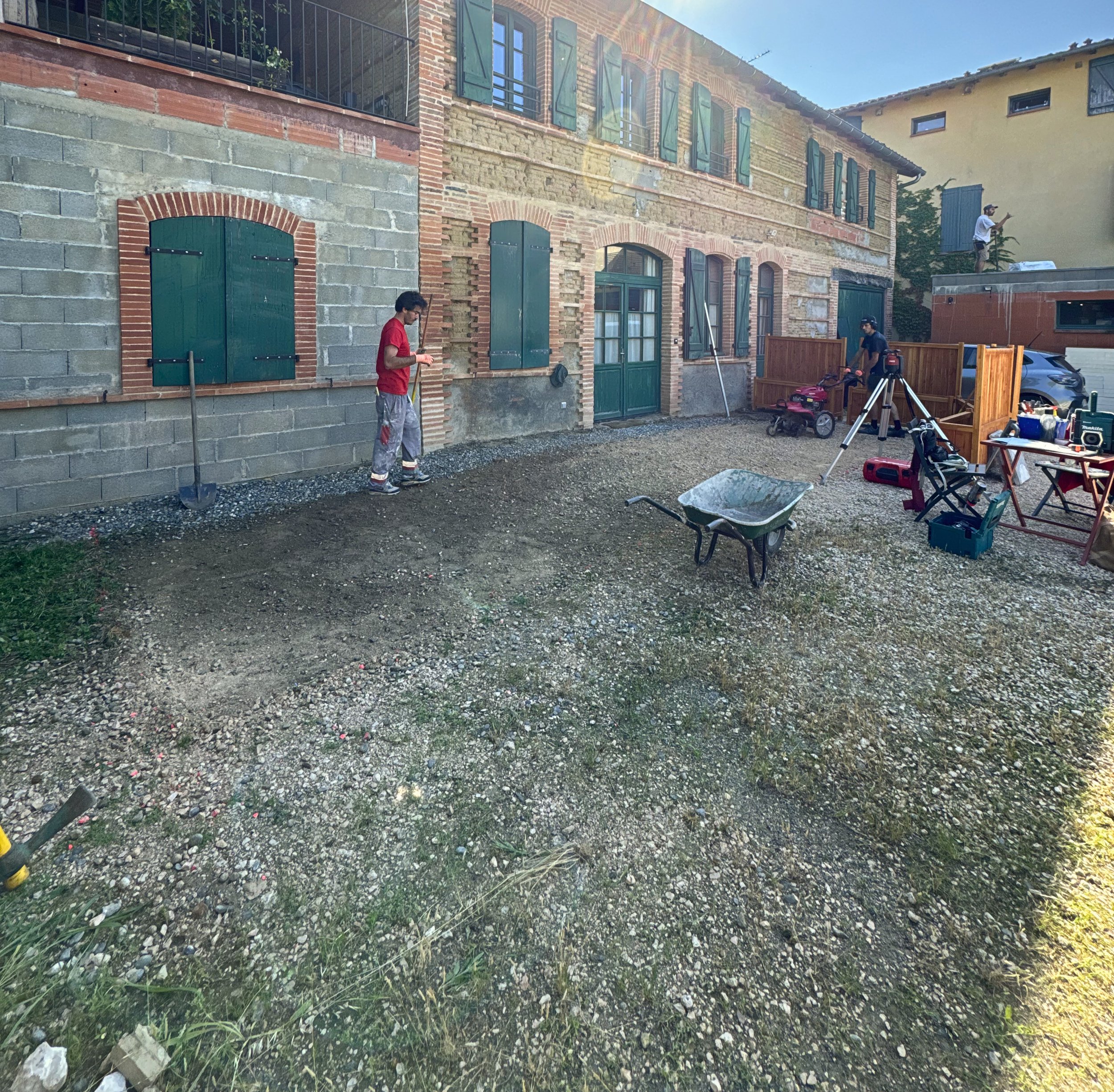 Travaux de construction en extérieur devant une maison ancienne avec des ouvriers, outils, et matériaux.
