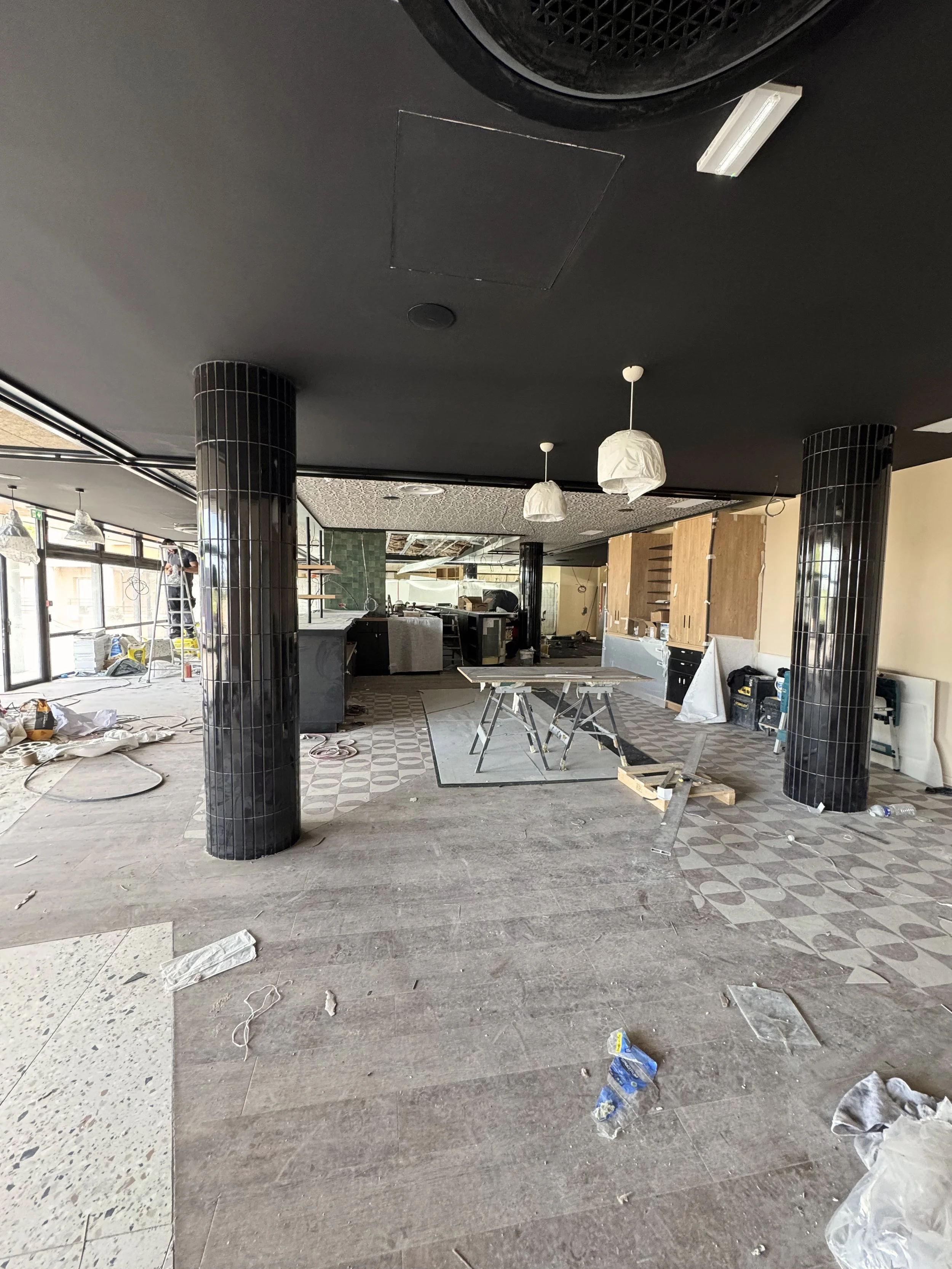 Intérieur d'un restaurant ou café en cours de rénovation ou construction, avec des matériaux, des outils et des meubles en désordre.
