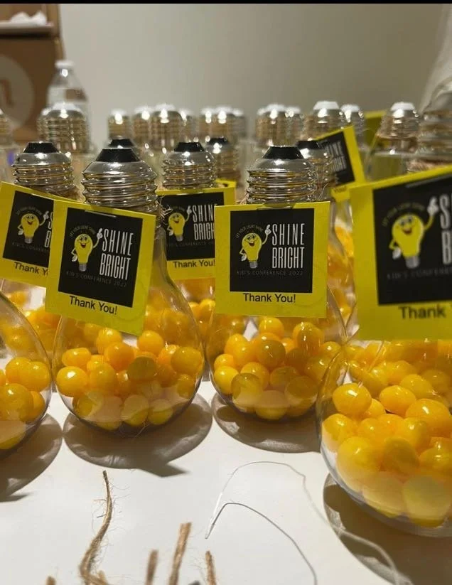 Clear plastic bottles filled with yellow and orange gumballs, tagged with black and yellow labels reading 'SHINE BRIGHT' and 'Thank You!'