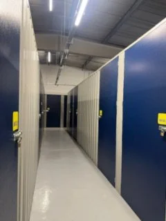 Long corridor in a storage facility with blue and beige lockers on the sides and overhead lighting