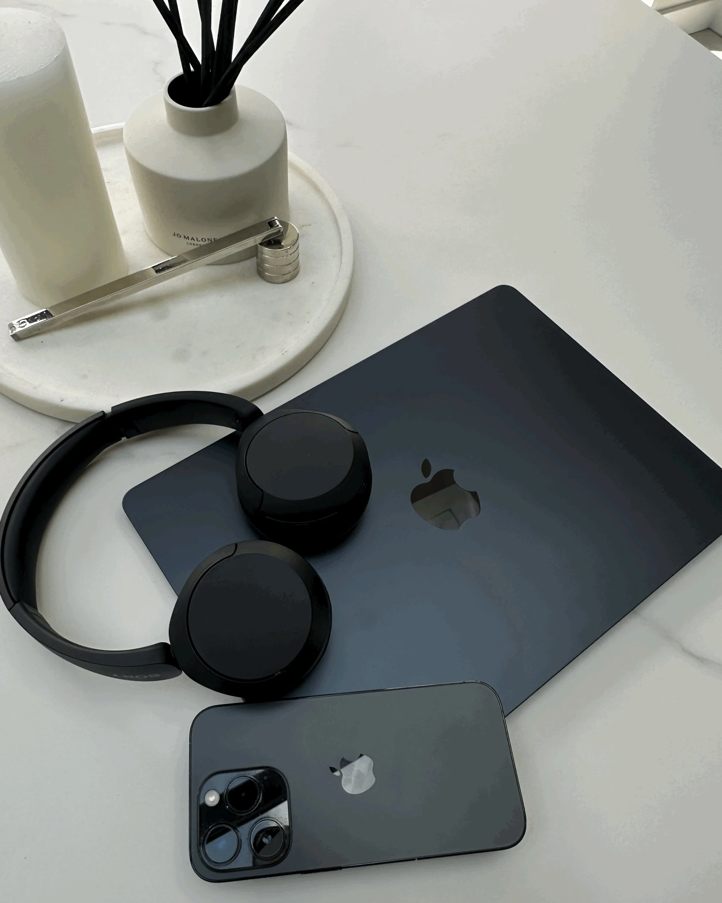 Close-up of a workspace with a smartphone, headphones, a MacBook laptop, and decorative items on a white table.