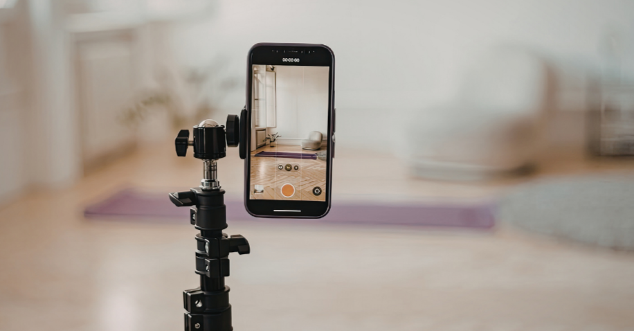 Smartphone mounted on a tripod recording a room with a yoga mat and exercise ball visible in the background.