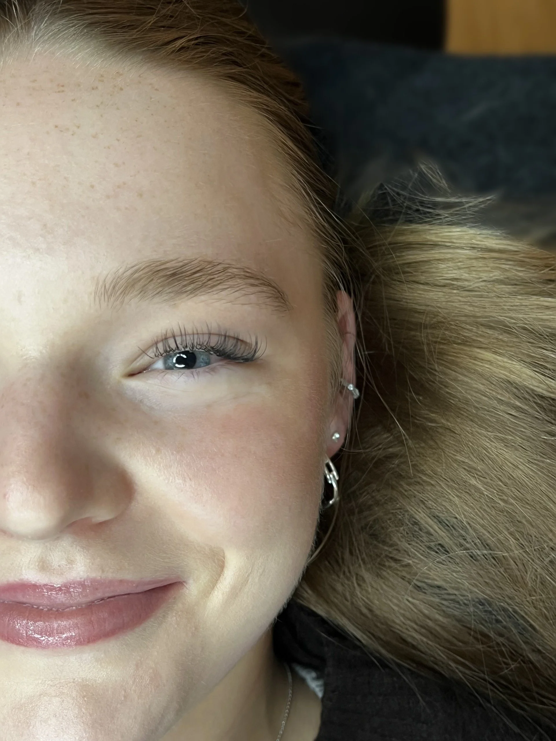 Close-up of a woman's face with blonde hair, blue eye, and earrings, lying down.