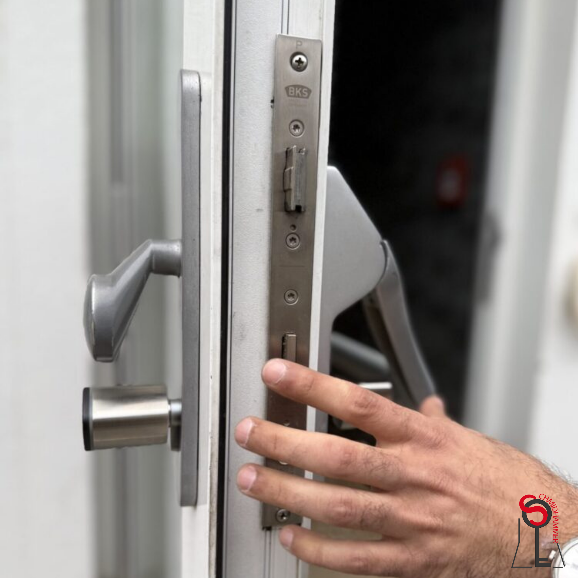 A person's hand touching a metal door latch on a door with a handle and lock mechanism.