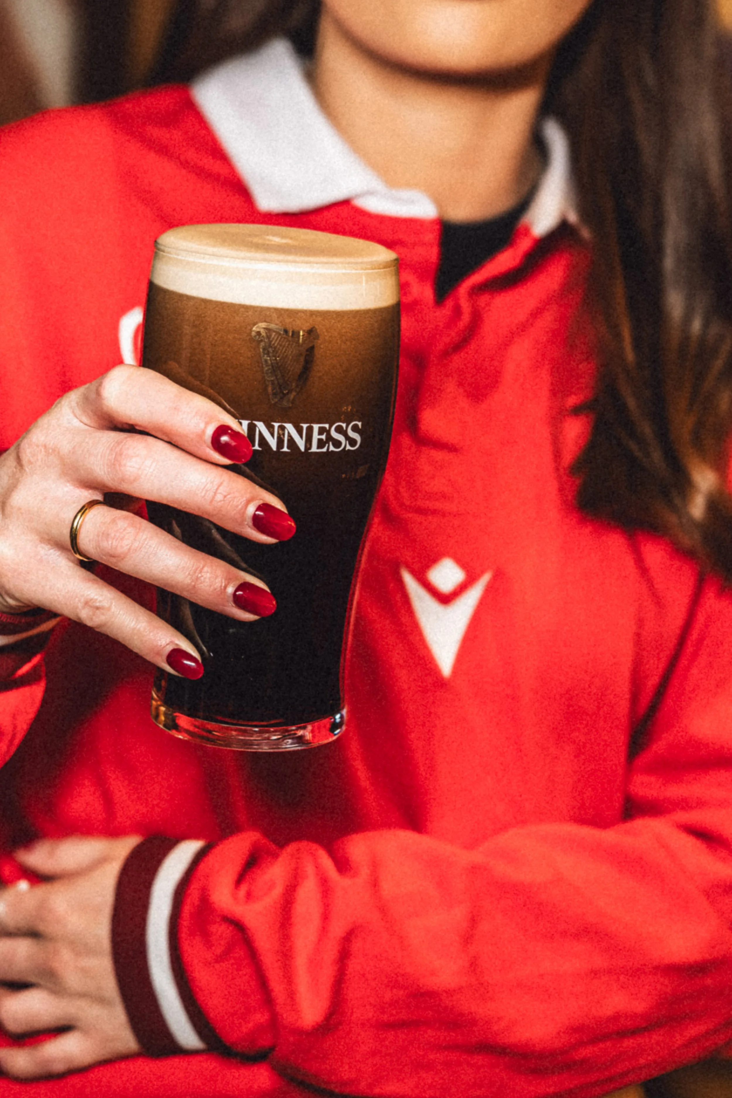 A woman in a red jacket holding a pint of Guinness beer with a foamy head.