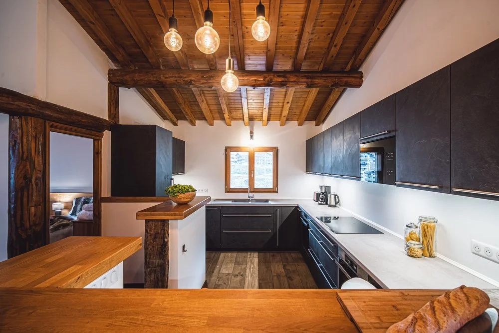 Modern kitchen with wooden ceiling, black cabinets, white countertop, and pendant lights.