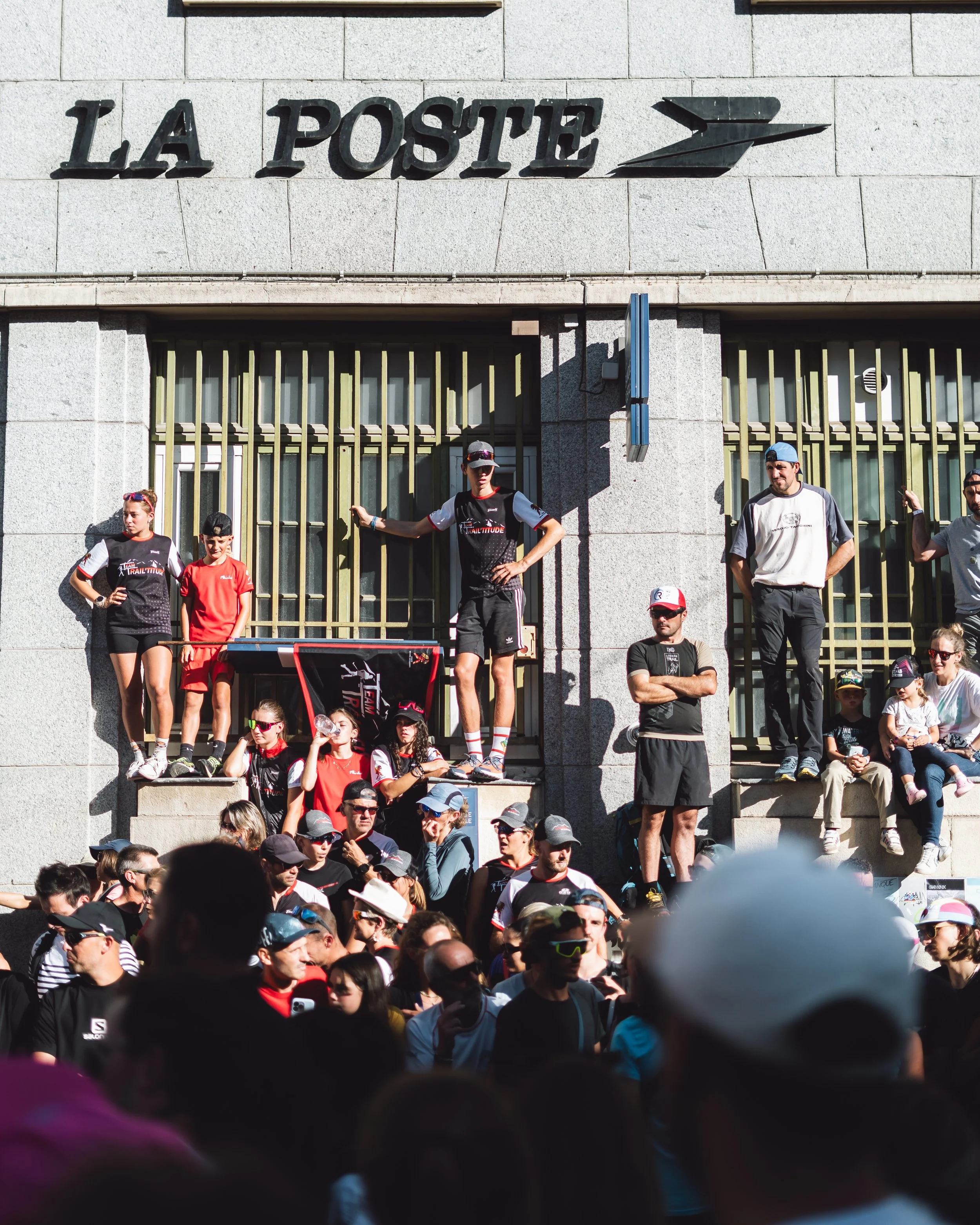 People gathered in front of La Poste building, some standing on ledges and others in a crowd, during an outdoor event or protest.