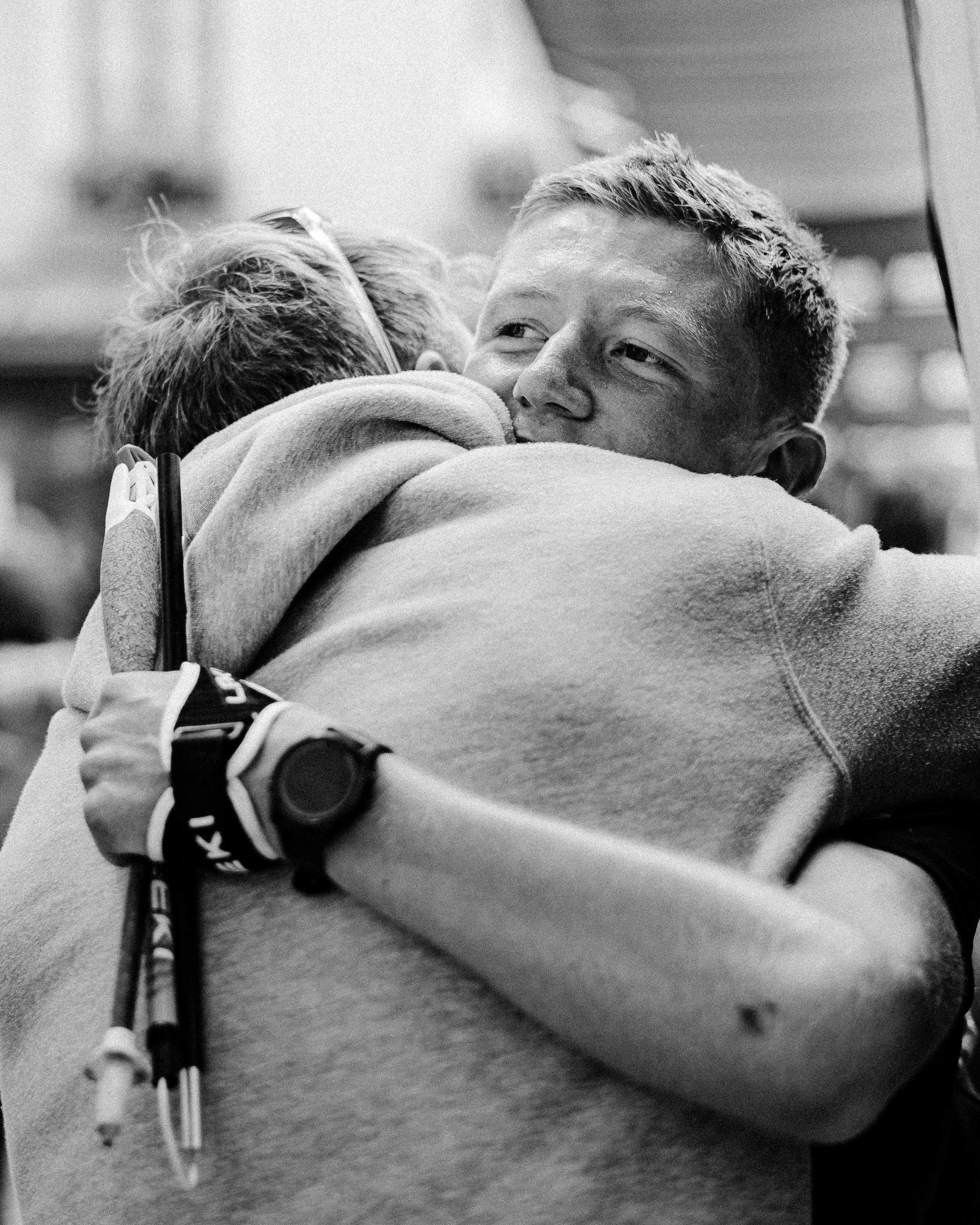 Two people hugging, one wearing a hoodie, inside a public space.