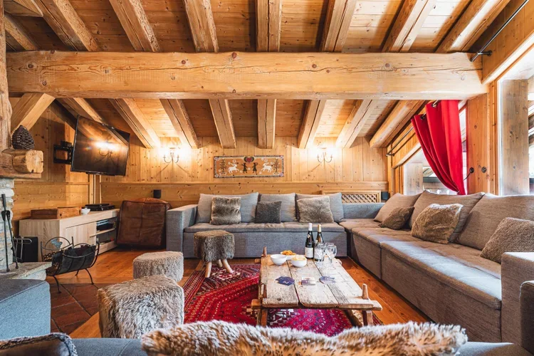 Cozy living room with wooden walls and ceiling, large sectional sofa, coffee table with drinks, a television, and red curtains.
