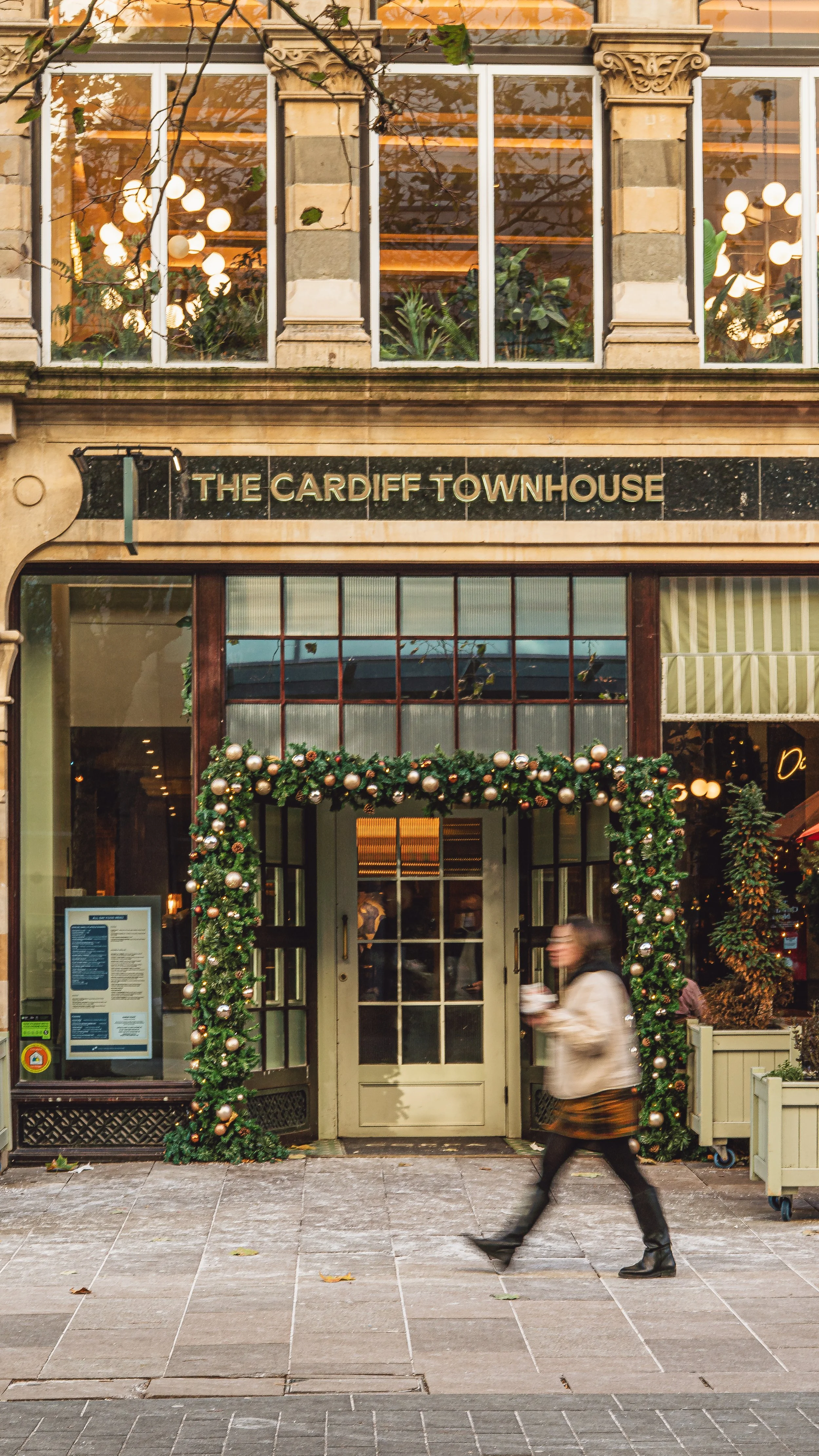 The entrance of The Cardiff Townhouse decorated with Christmas garland and ornaments, with a woman walking past holding a drink.