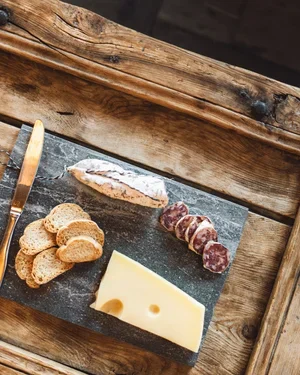Cheese, two types of sausage, bread slices, and a knife on a cutting board.