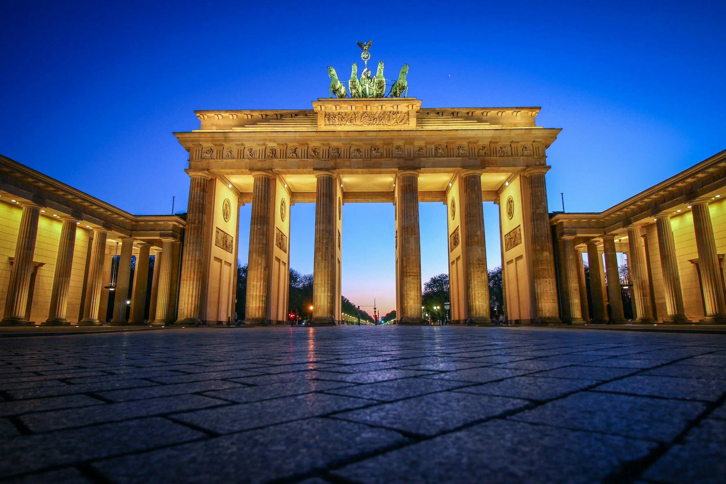 Night view of the Brandenburg Gate in Berlin, Germany, illuminated with warm lights, with a clear blue sky above.