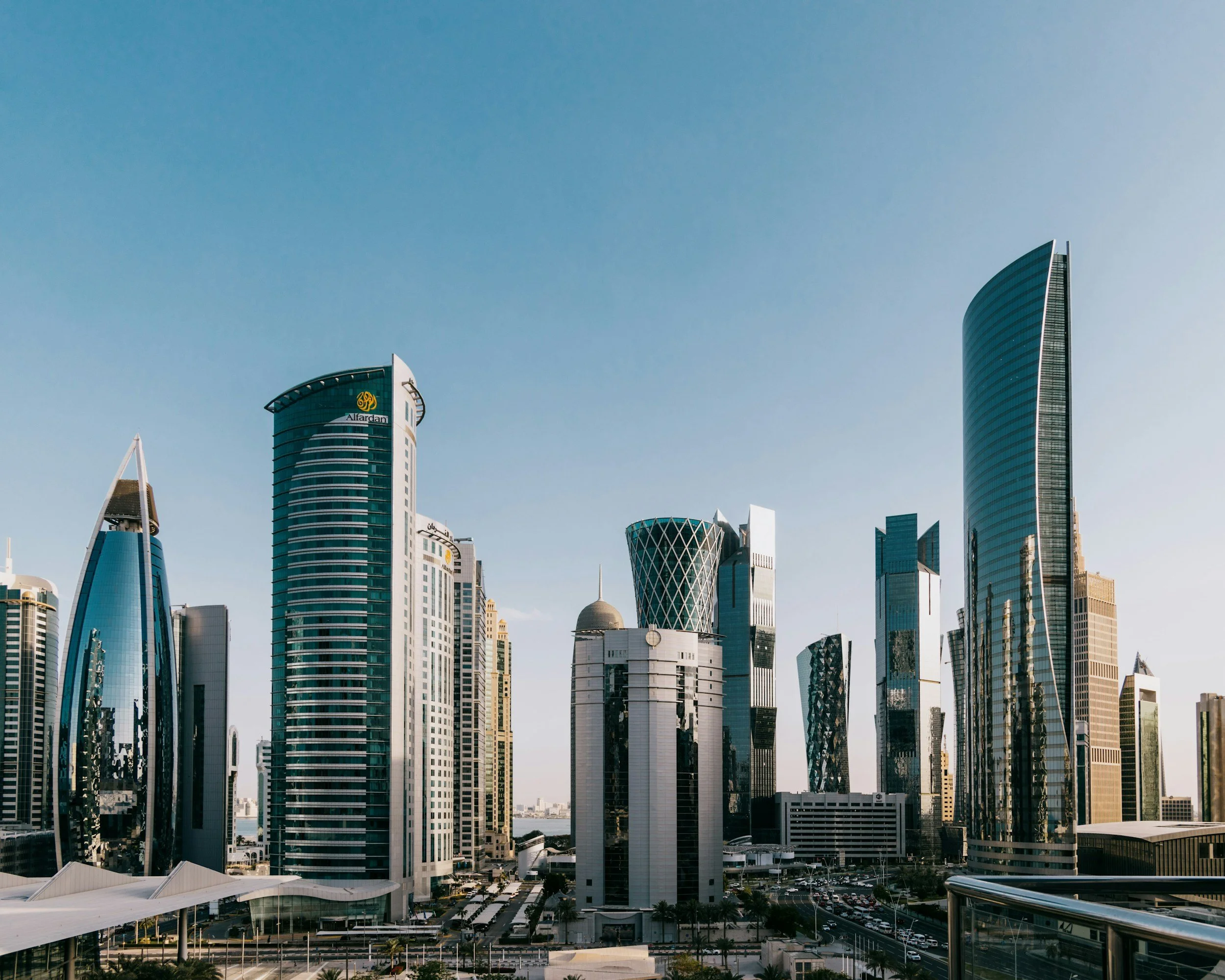 A cityscape with modern skyscrapers in Doha, Qatar, under a clear blue sky, featuring the Alfardan Tower among other high-rise buildings.