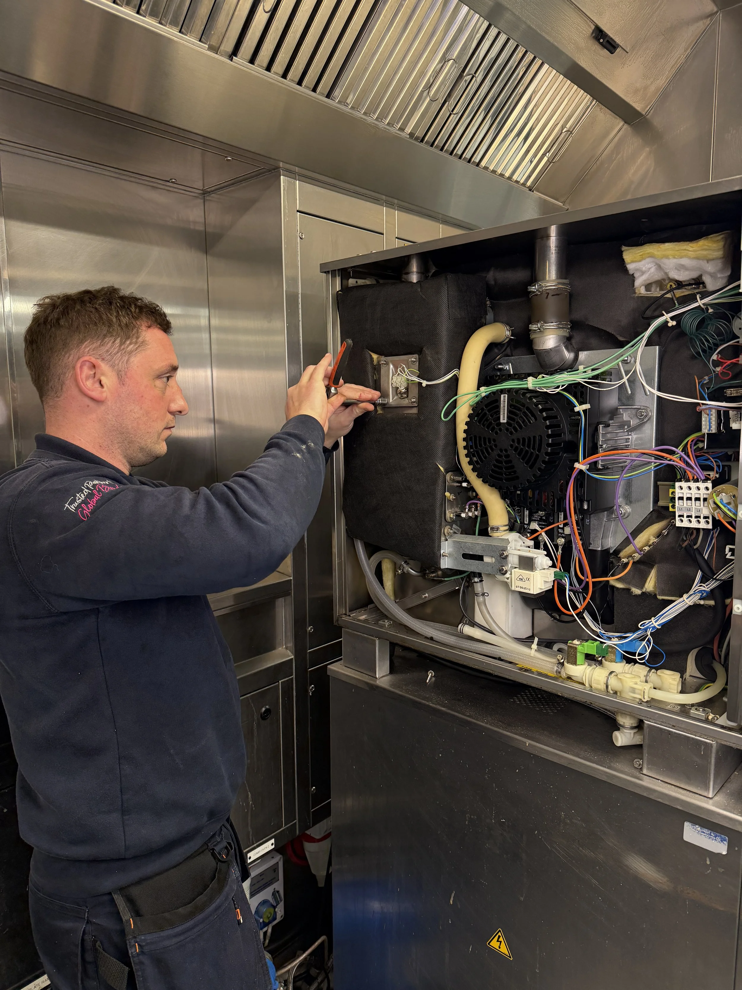 A technician inspecting electrical and mechanical components inside a stainless steel industrial machine in a professional setting.