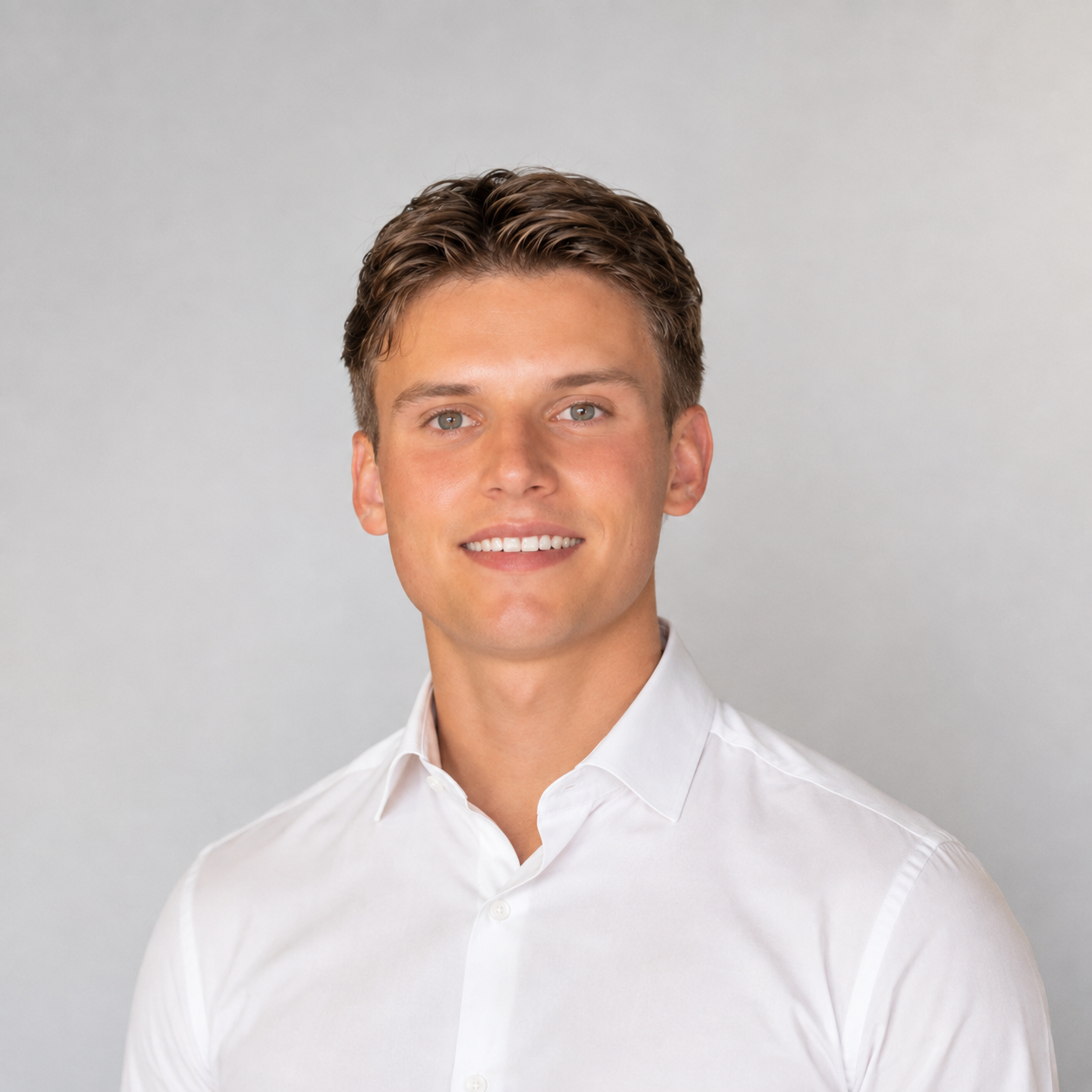 Portrait of a young man with short brown hair, wearing a dark navy polo shirt, standing against a gray background.