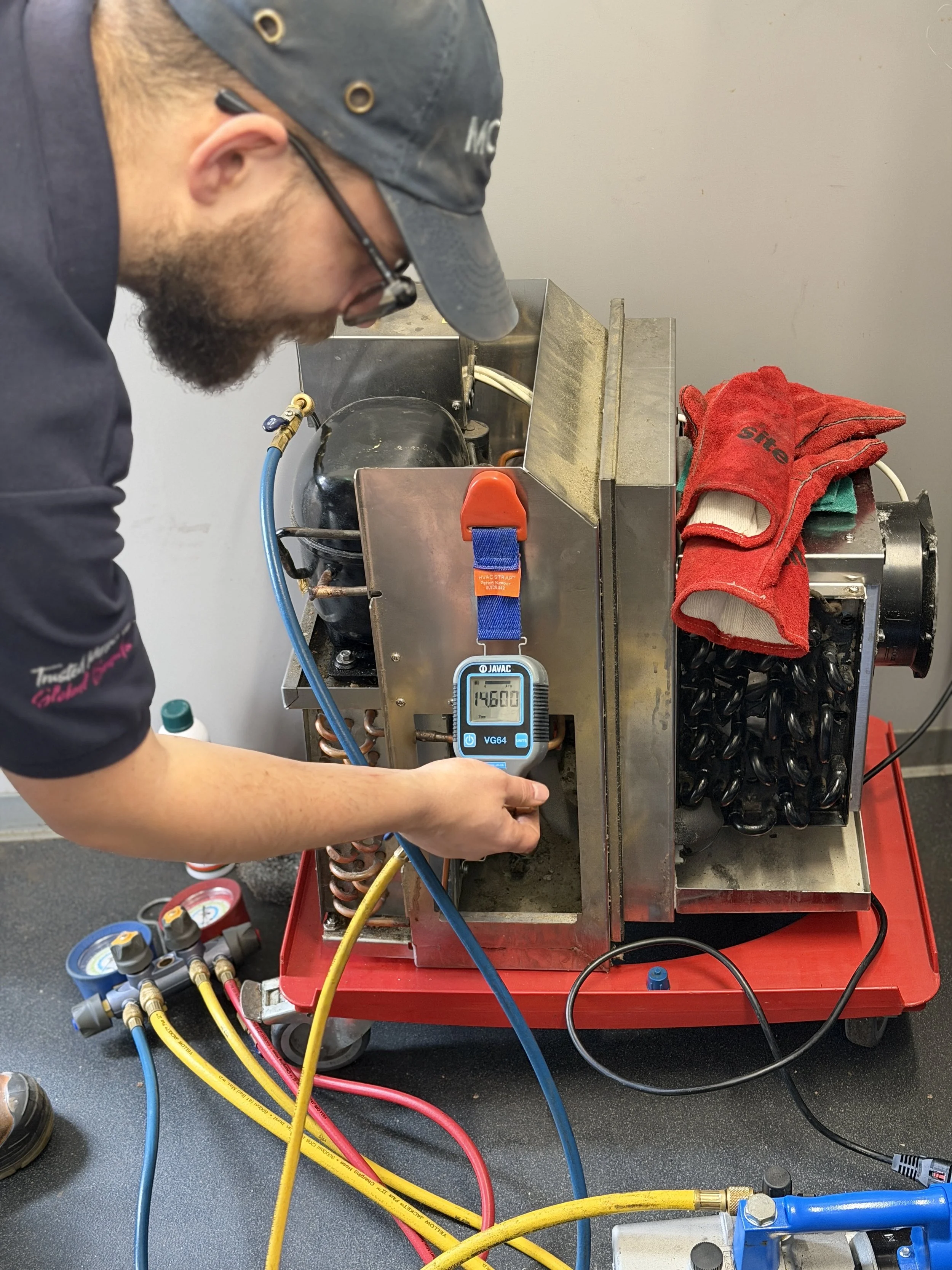 Technician checking refrigerant pressure gauge on HVAC system with hoses connected