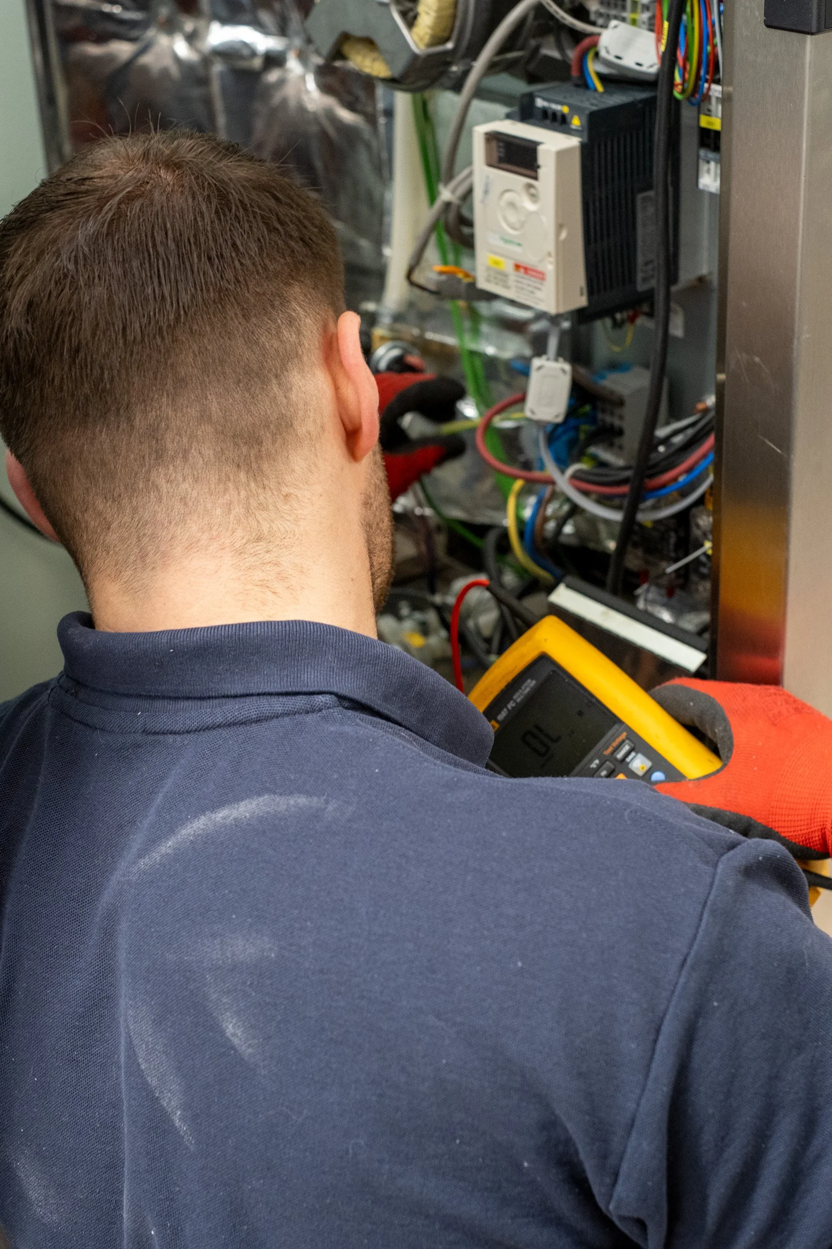 A technician is working on electrical wiring inside an electrical panel, using a multimeter to test the circuit.