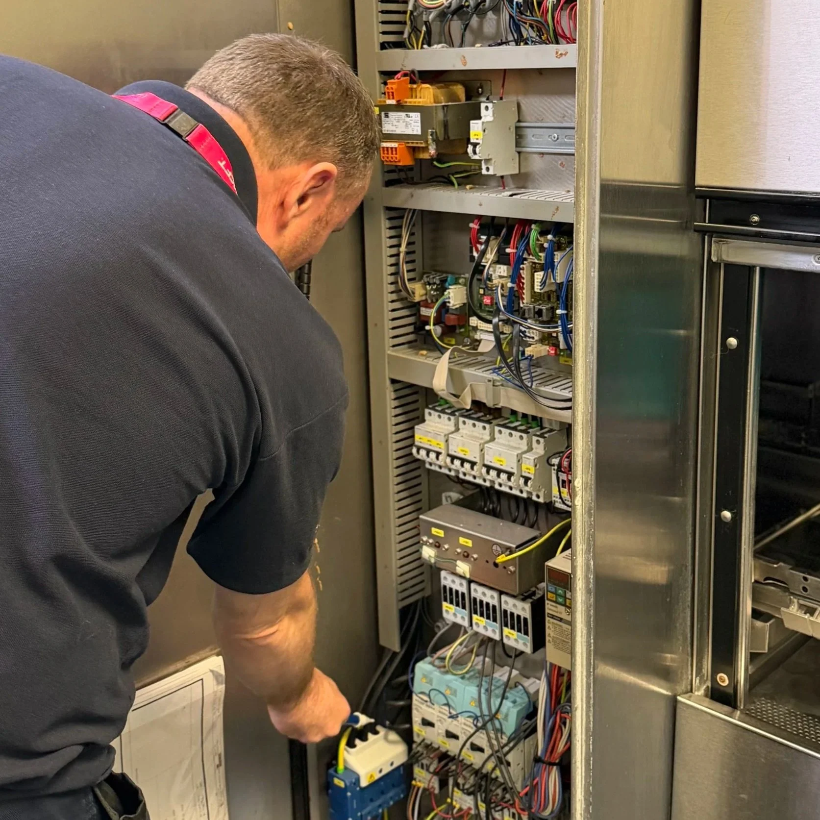A technician working on an electrical control panel, fixing or inspecting the various wires and components inside, in an industrial or maintenance setting.