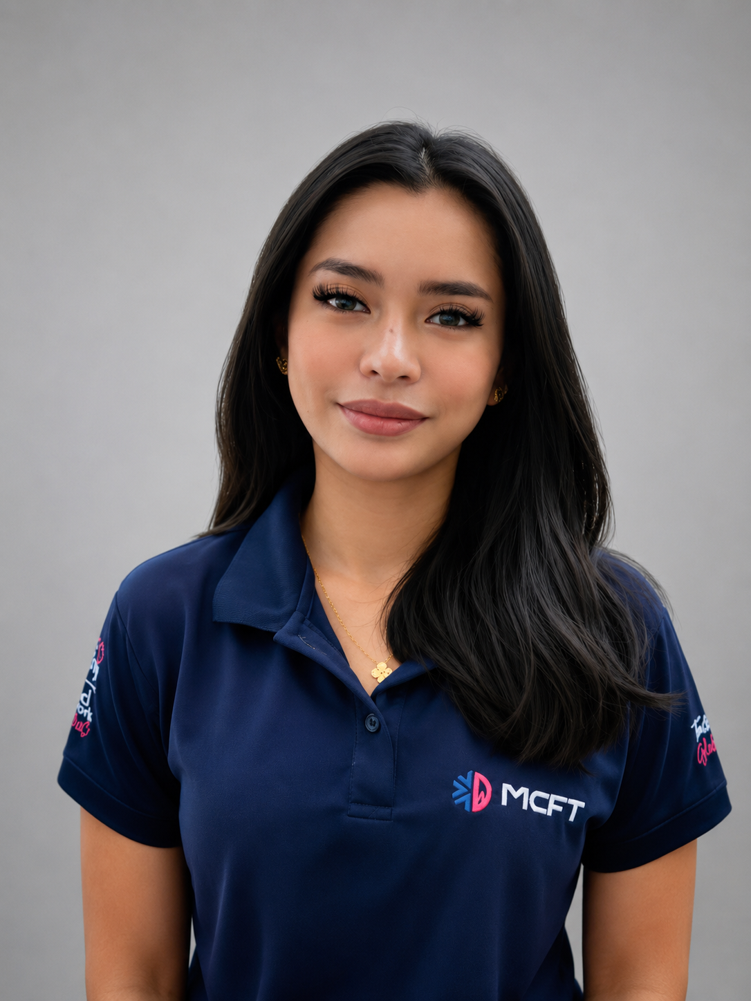 A young woman with long black hair, wearing a navy blue polo shirt with logos, standing against a plain gray background.