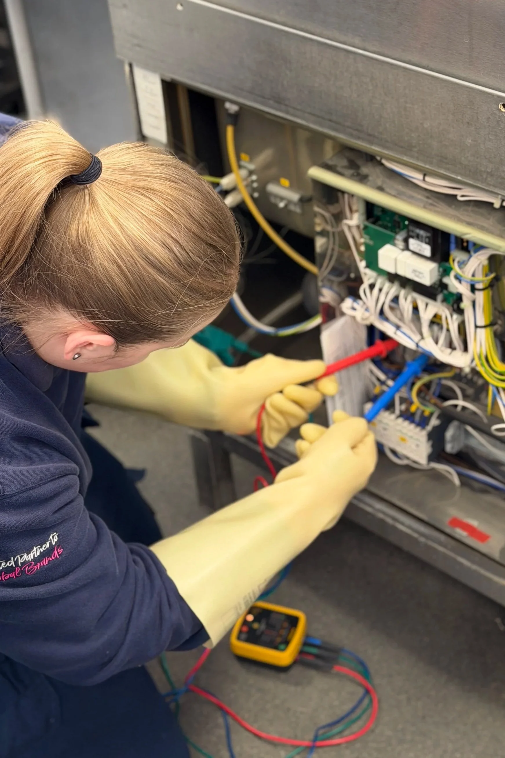 A woman working on electrical wiring inside an electrical panel, using a multimeter to check voltage.