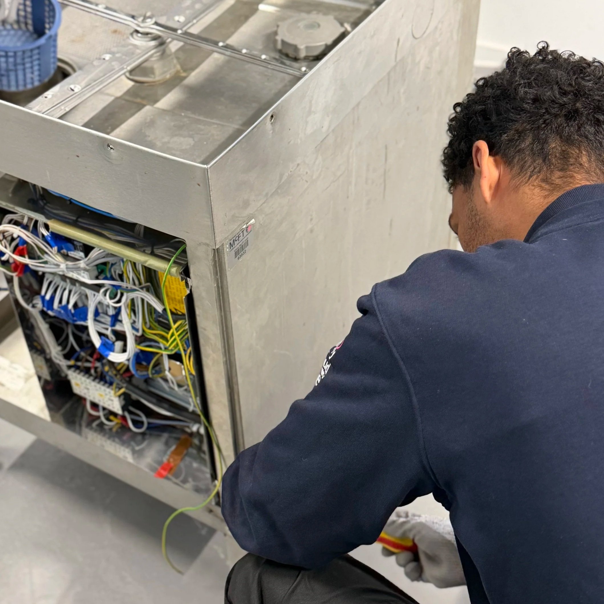 Man working on electrical wiring inside an open electrical panel with numerous wires.