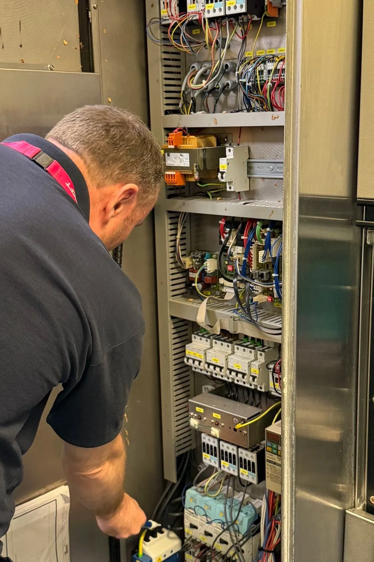 A technician working inside an electrical control panel with various wires and components.