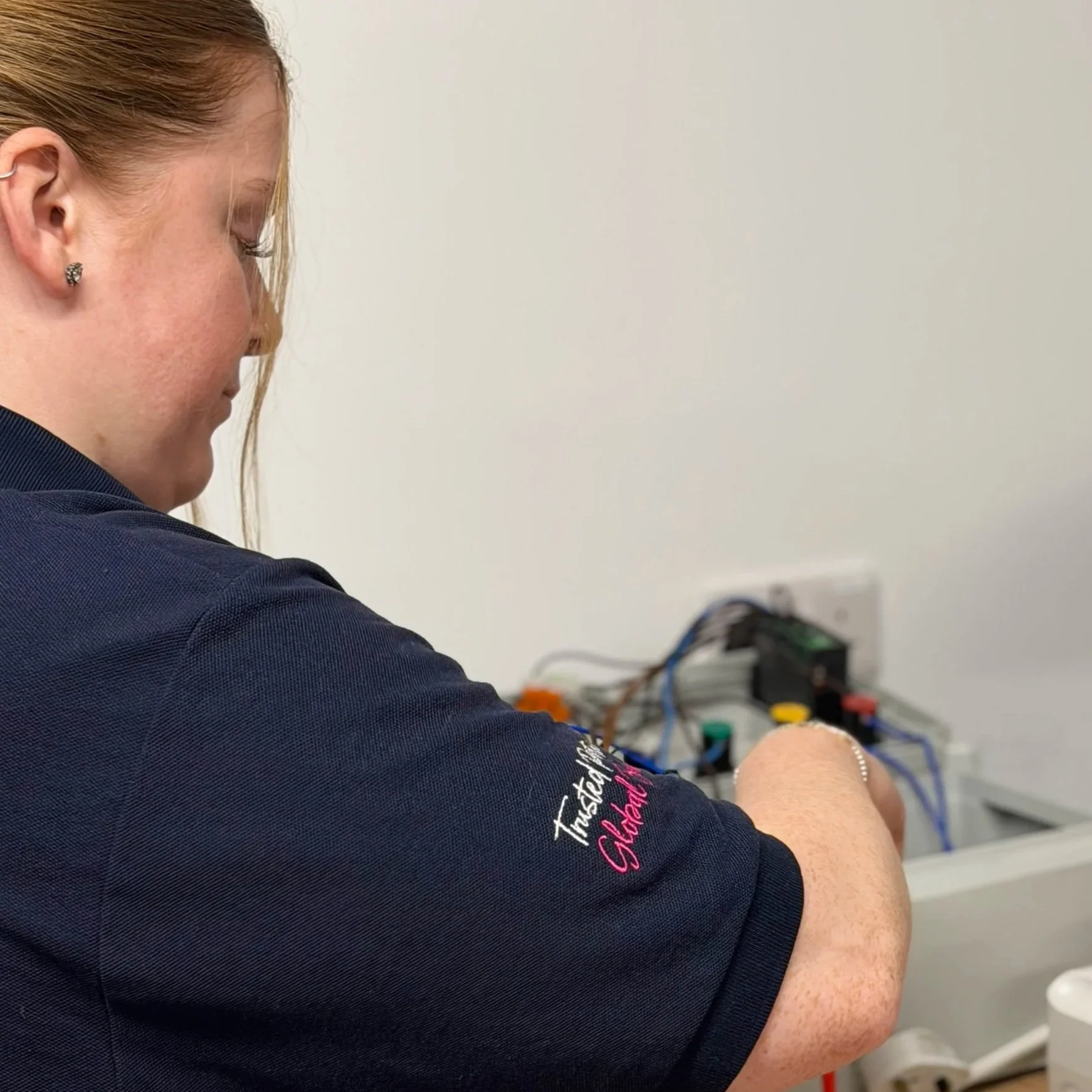 Close-up of a woman with red hair and earrings, sitting with her eyes closed, in a medical or laboratory setting, with wires and electronic equipment nearby.