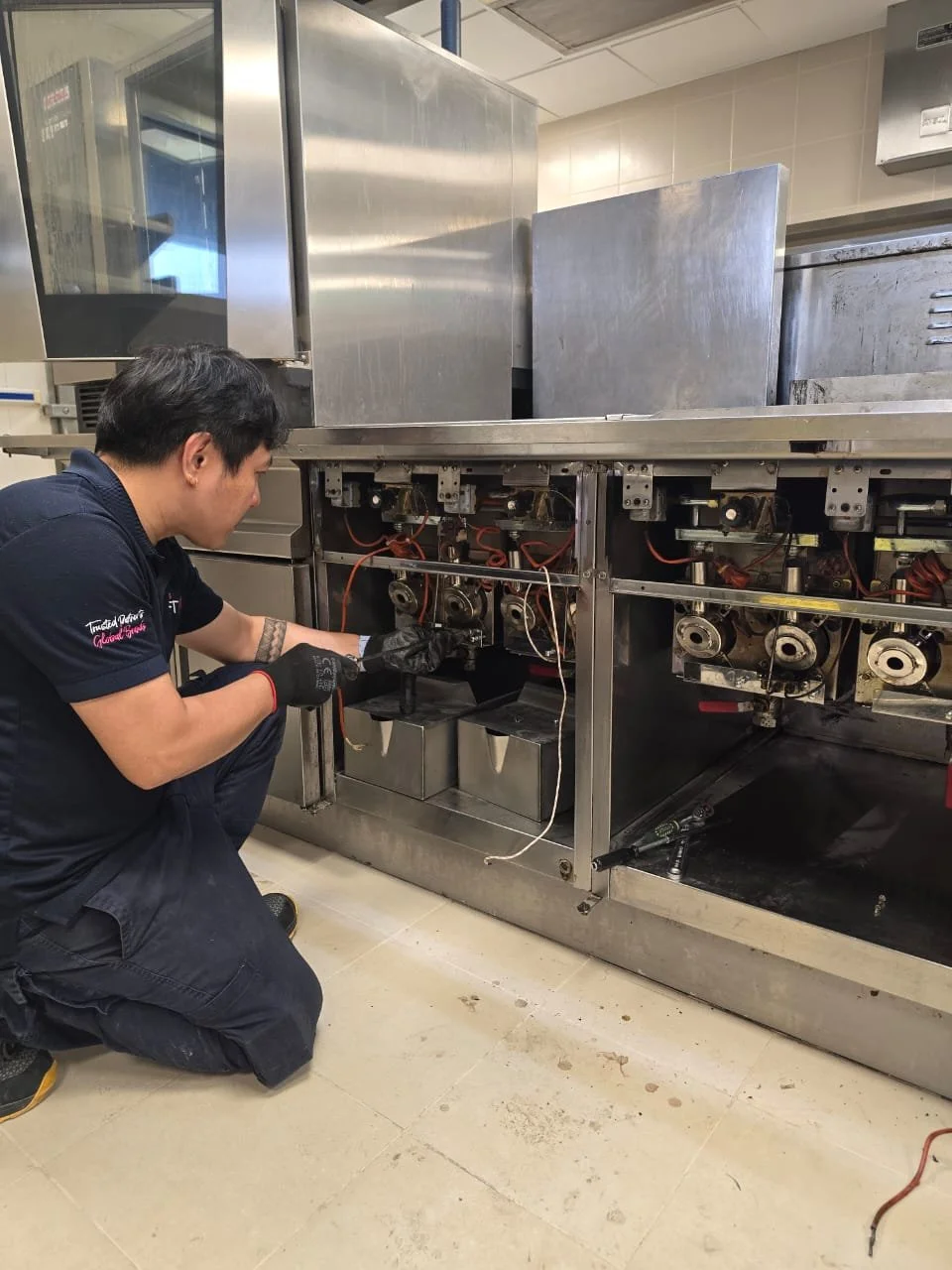 A technician repairing the internal components of a commercial kitchen appliance, possibly a dishwasher or oven, with the panel removed.