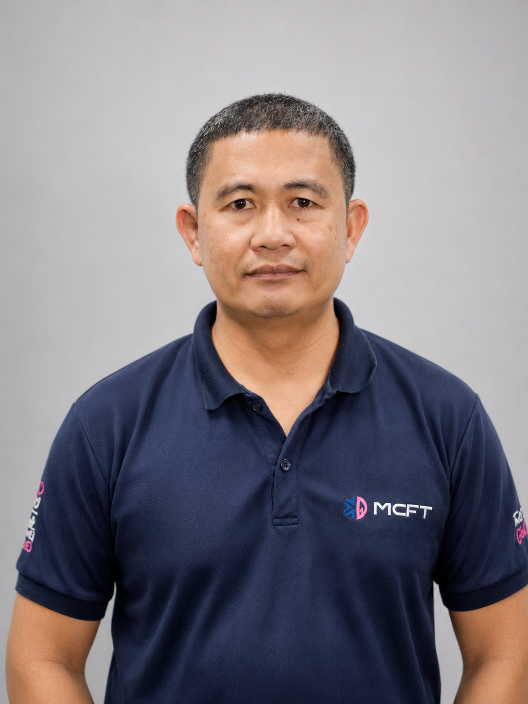 A man in a navy blue polo shirt standing against a plain gray background, looking directly at the camera.