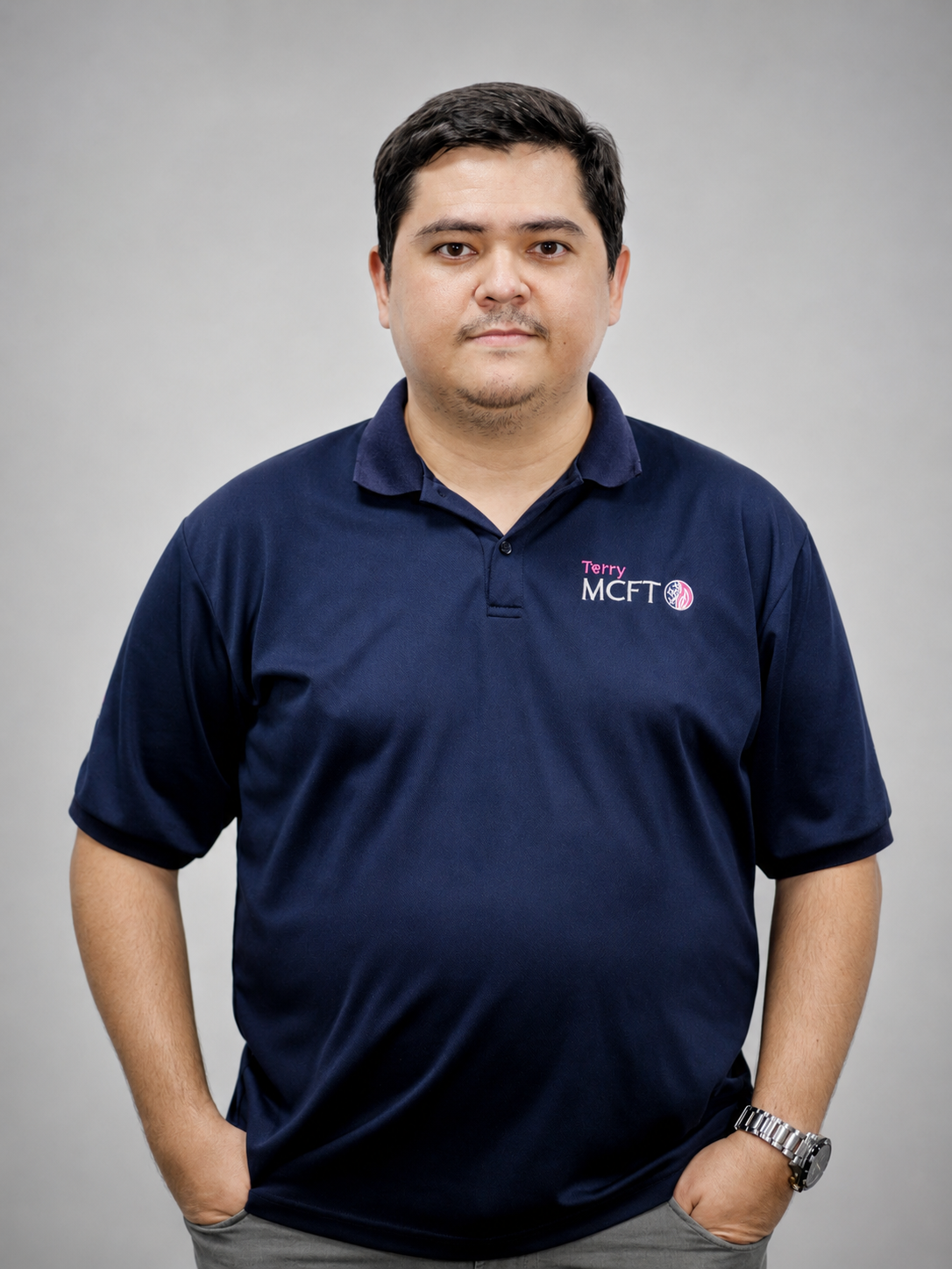 Man wearing navy polo shirt with 'Terry MCFT' embroidered on it, standing against a plain gray background, looking at the camera.