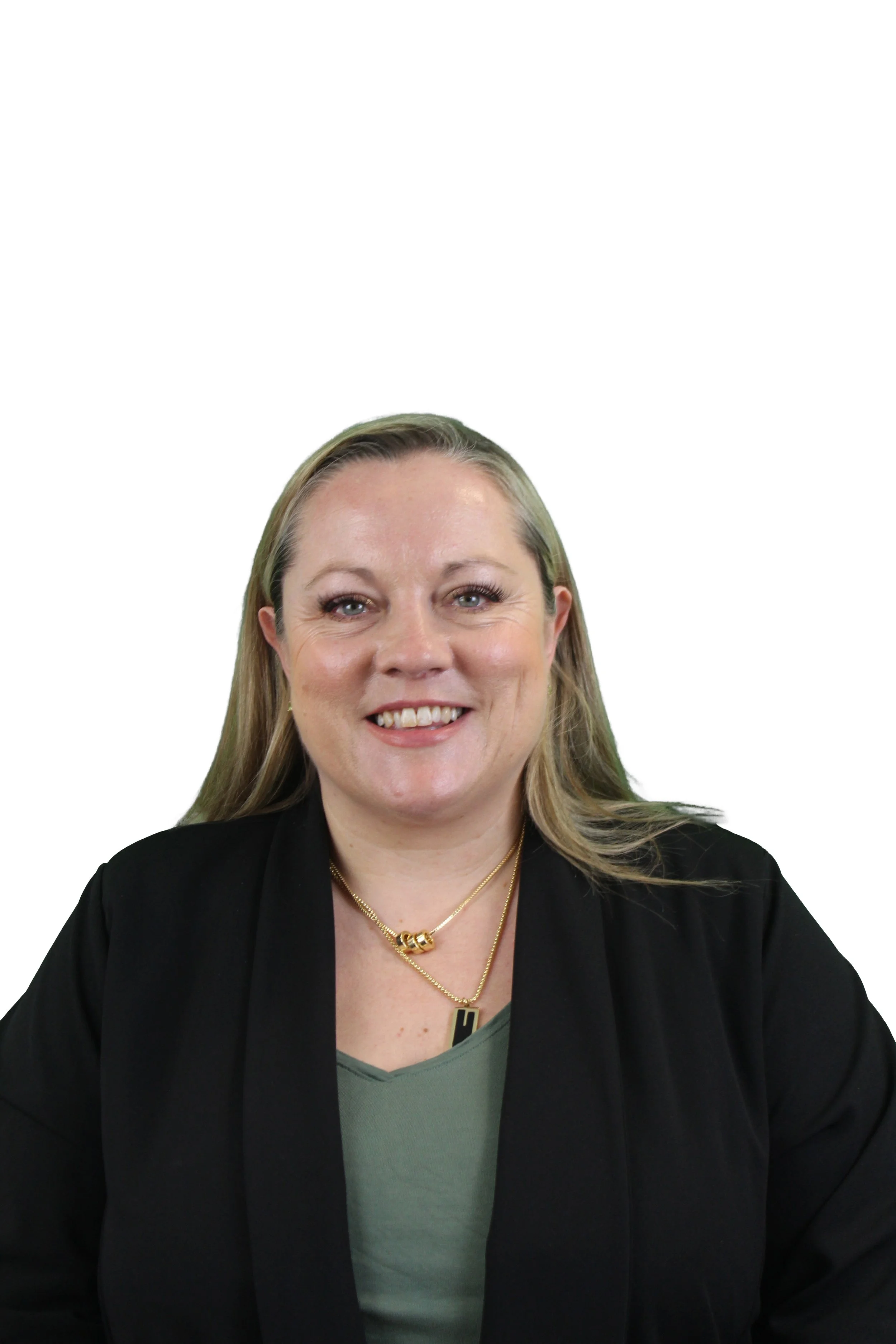 A woman with blonde hair smiling, wearing a black blazer, green shirt, layered gold necklaces, and sitting against a plain white background.
