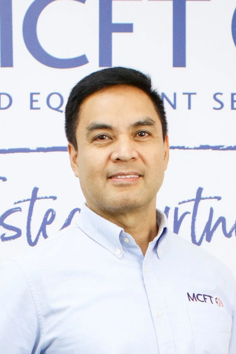 A man in a white button-up shirt standing in front of a backdrop with text, including the words "ICF" and "MCFT."