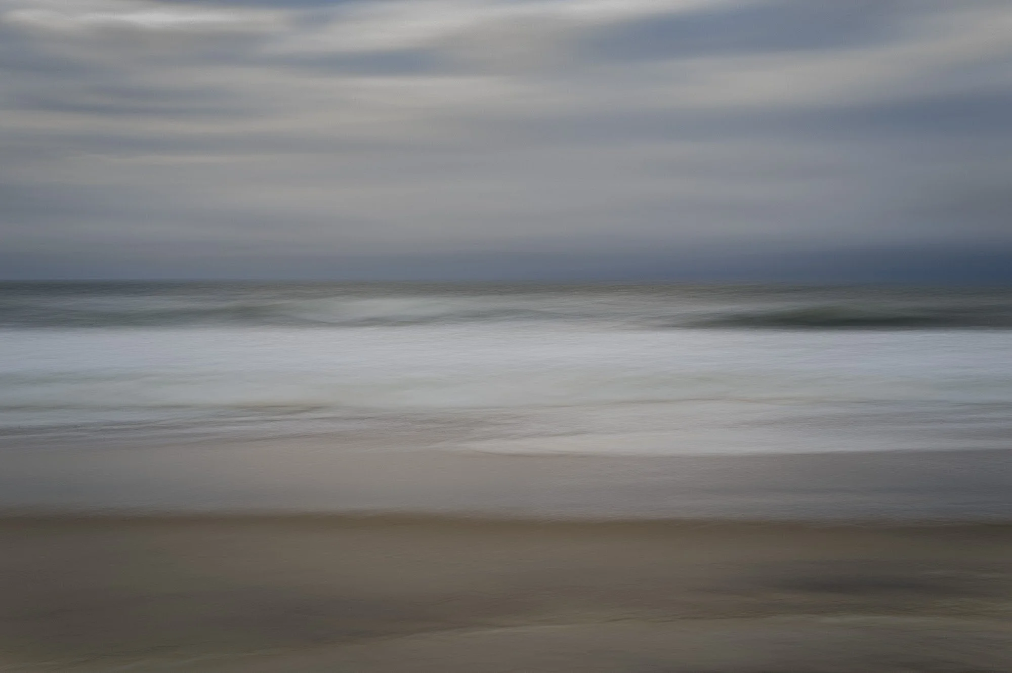 Blurred image of a beach with ocean waves and cloudy sky.