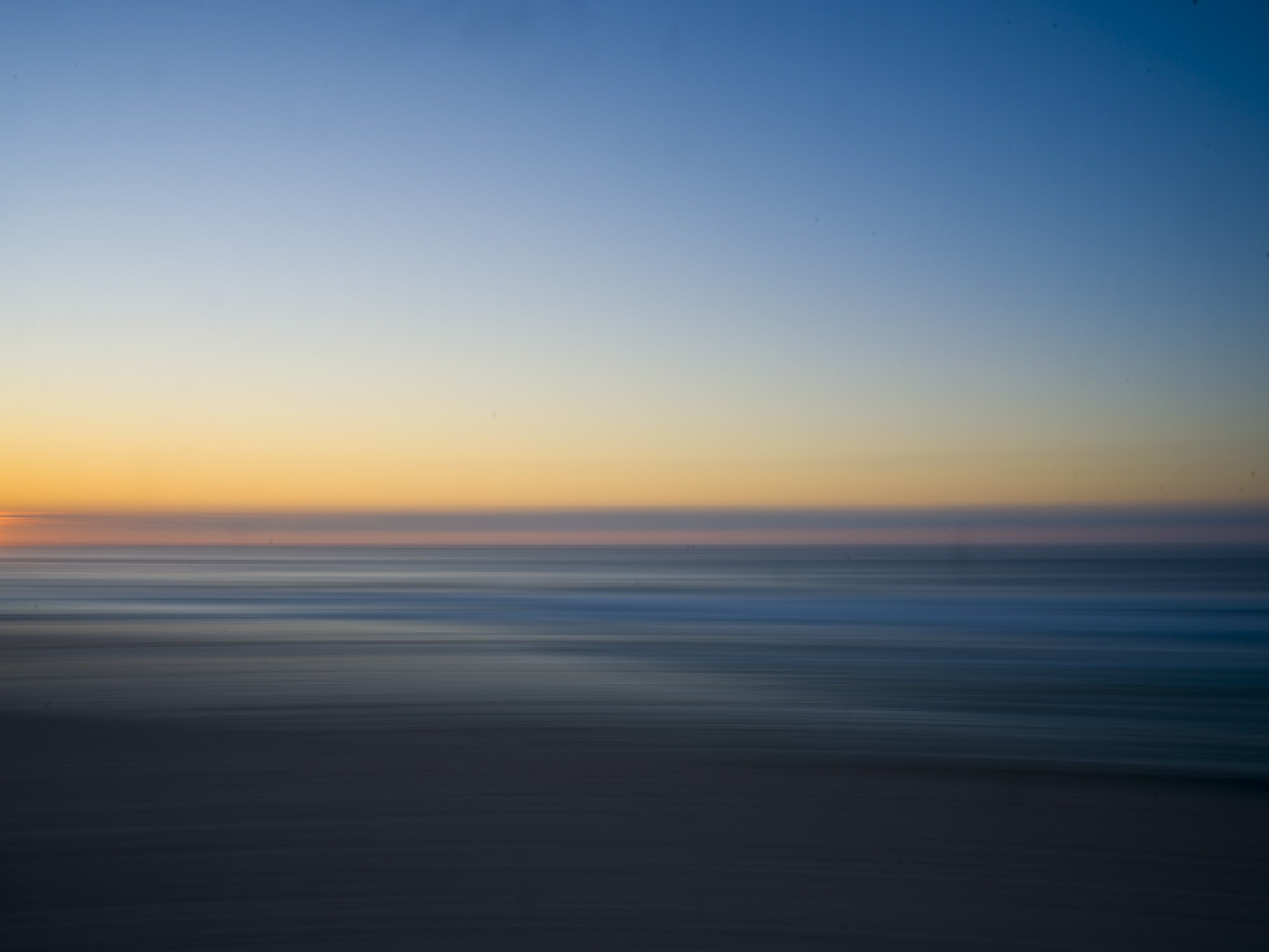 Blurry photo of a sunset over the ocean with a gradient sky from yellow to blue.