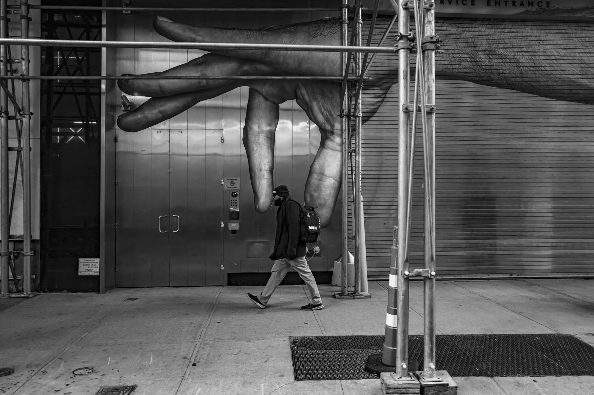 A person walking past scaffolding and a giant hand sculpture on a building's exterior wall.