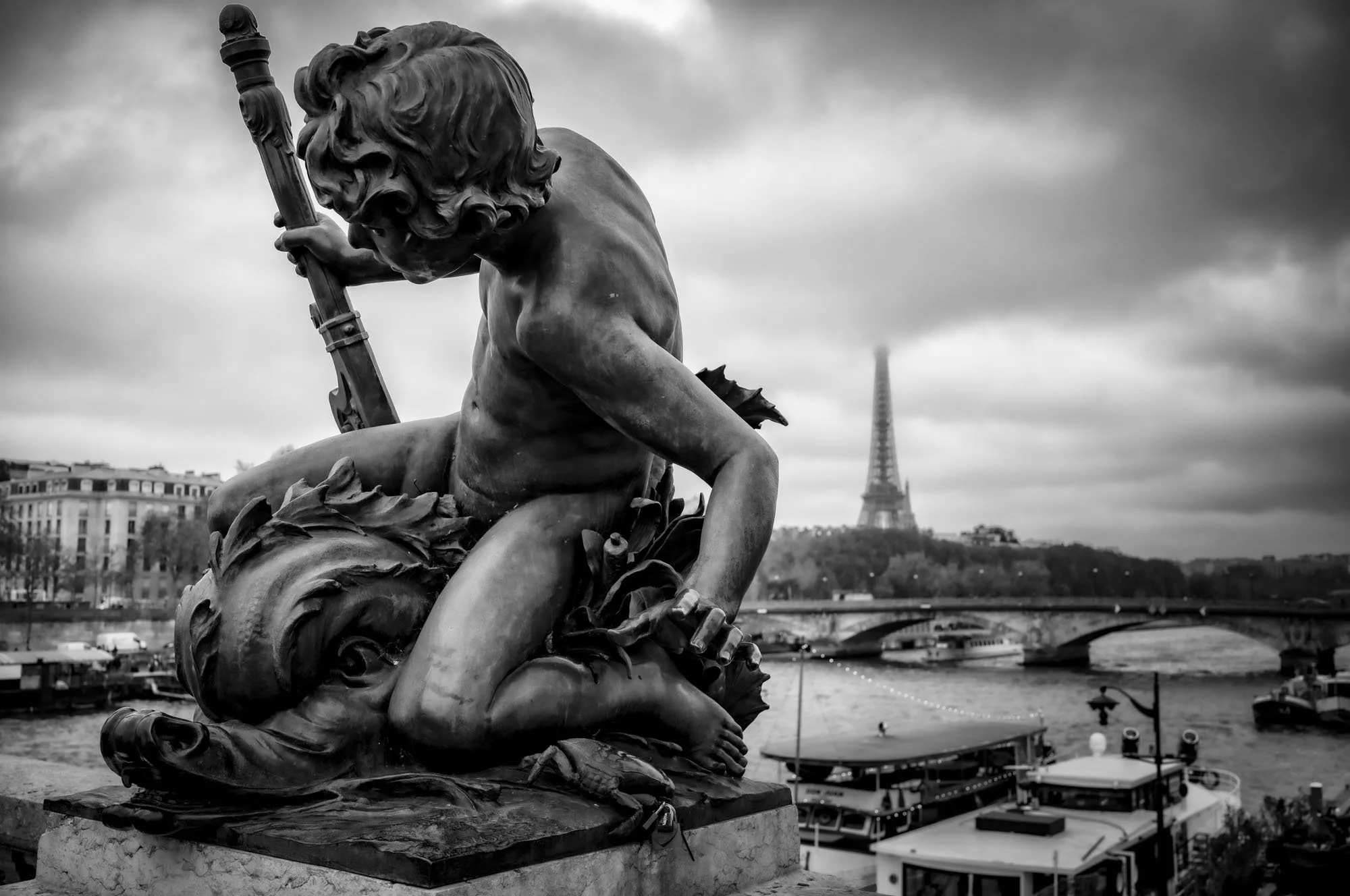 A black and white photo of a sculpture of a mythological figure with a trident on a pedestal, overlooking the Seine River in Paris with the Eiffel Tower in the background.