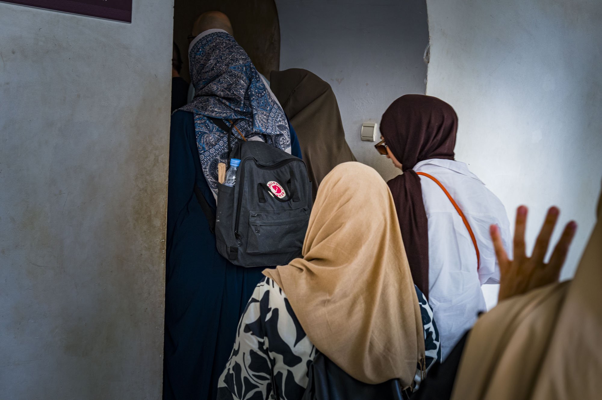 Five women wearing headscarves are gathered in a small, indoor space, engaged in conversation or activity.