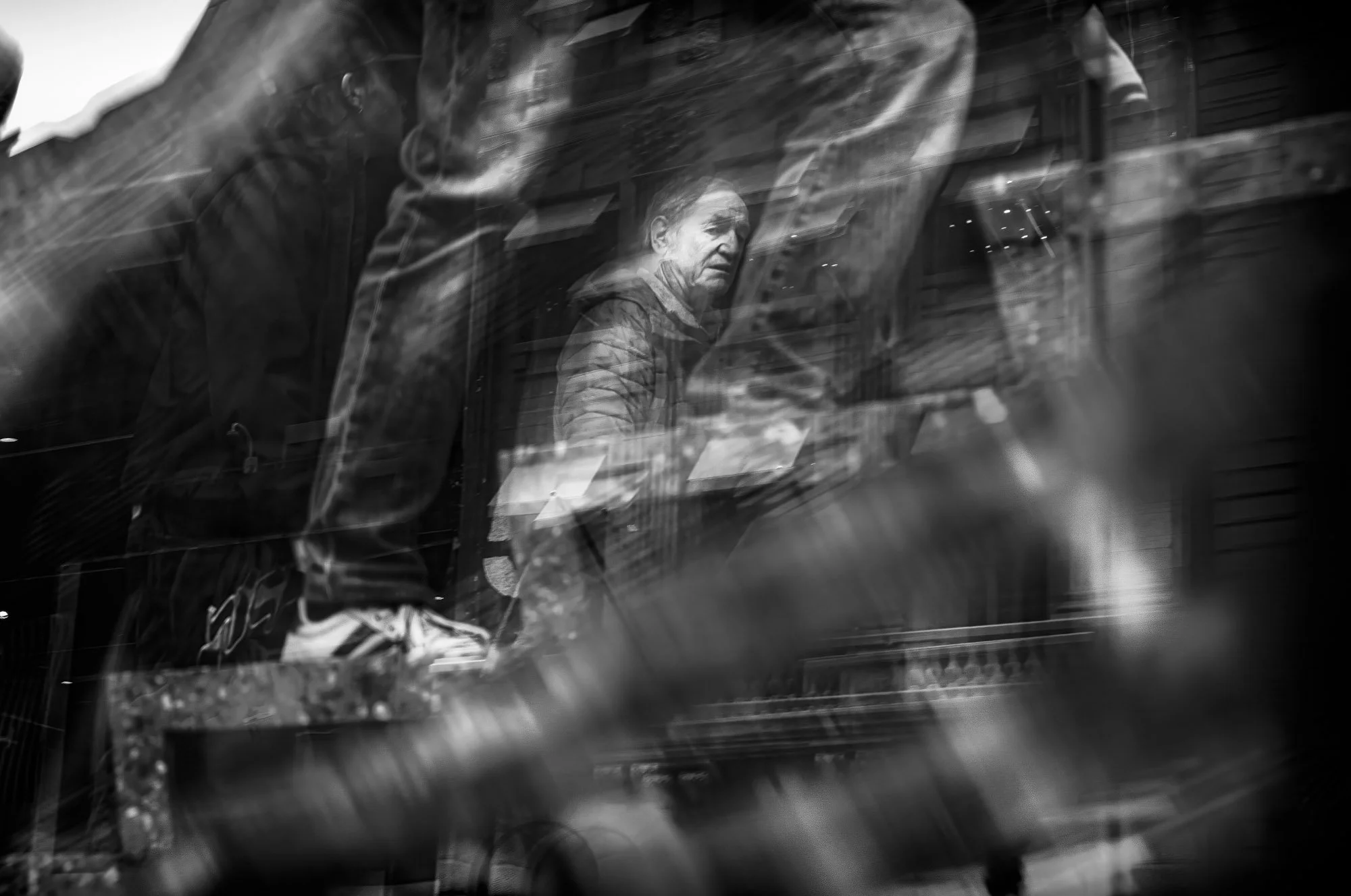 A black and white photo of a man seen through a glass window, with reflections and blurs creating an abstract effect.