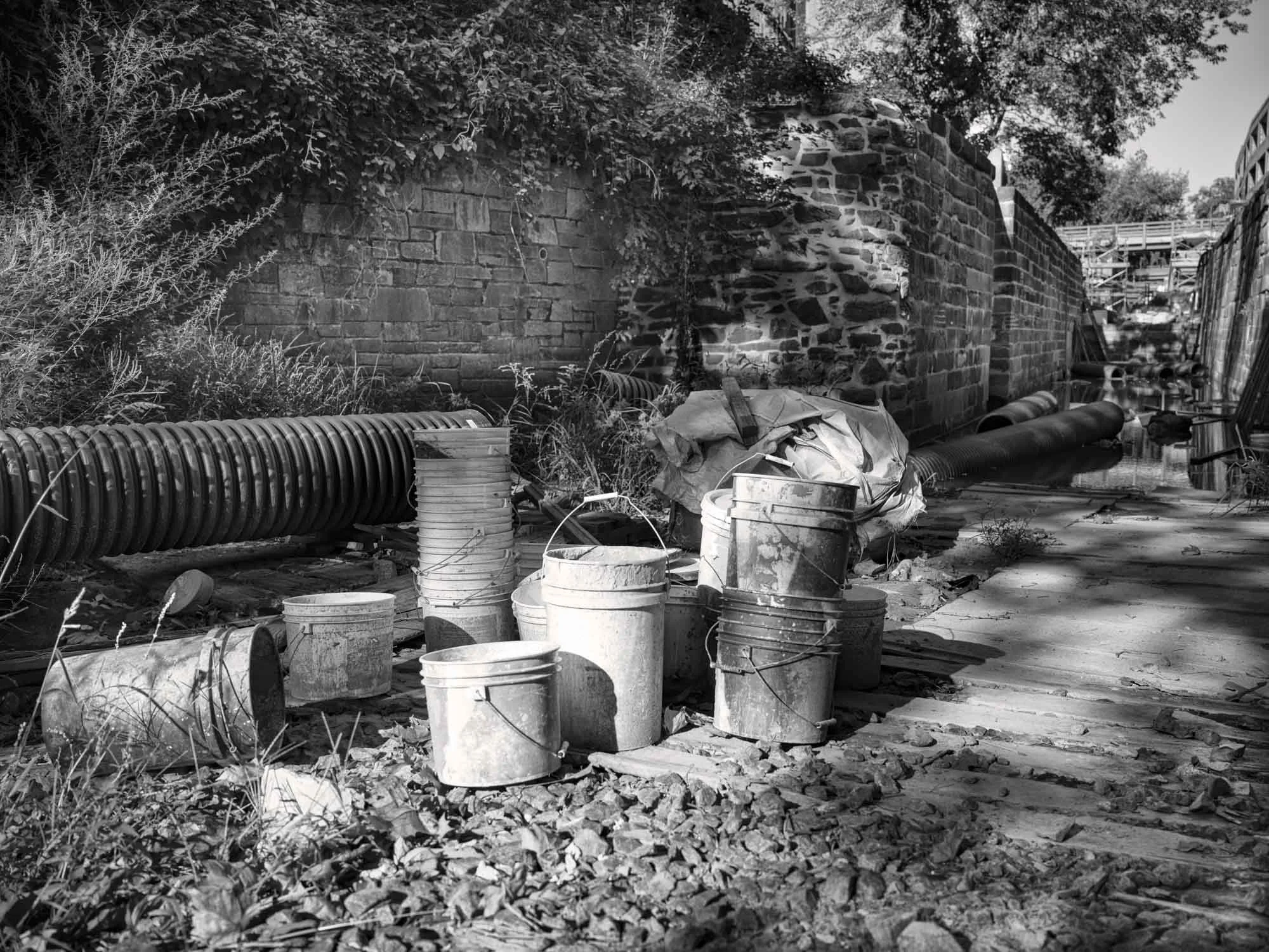 Construction site with buckets, pipes, debris, and a brick wall in the background.