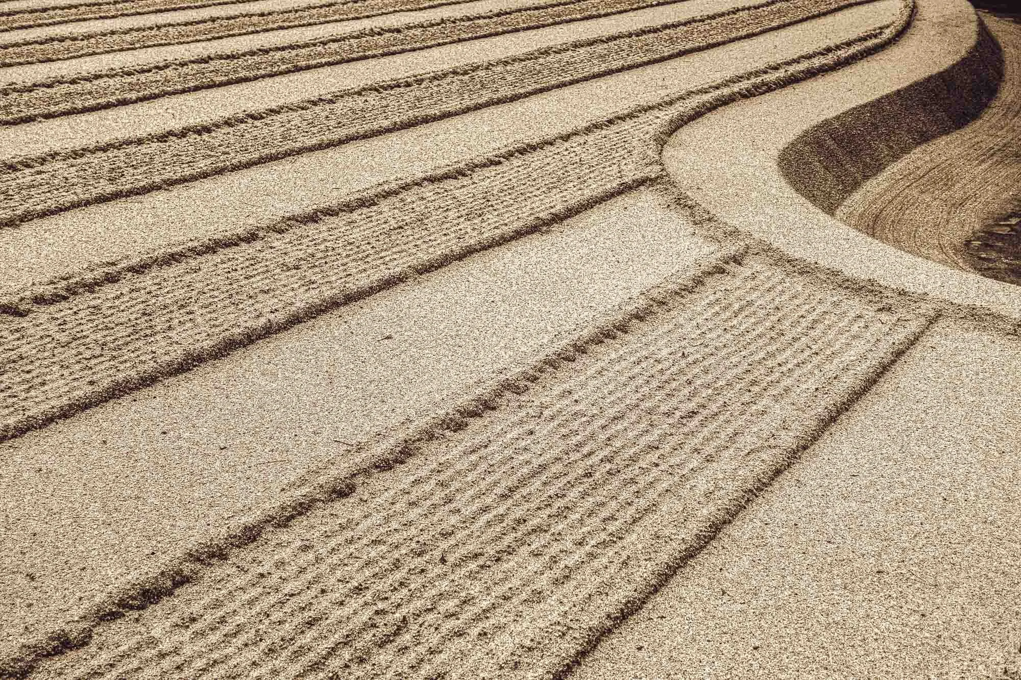 Close-up of sand with patterns and curved lines created by a rake or similar tool.