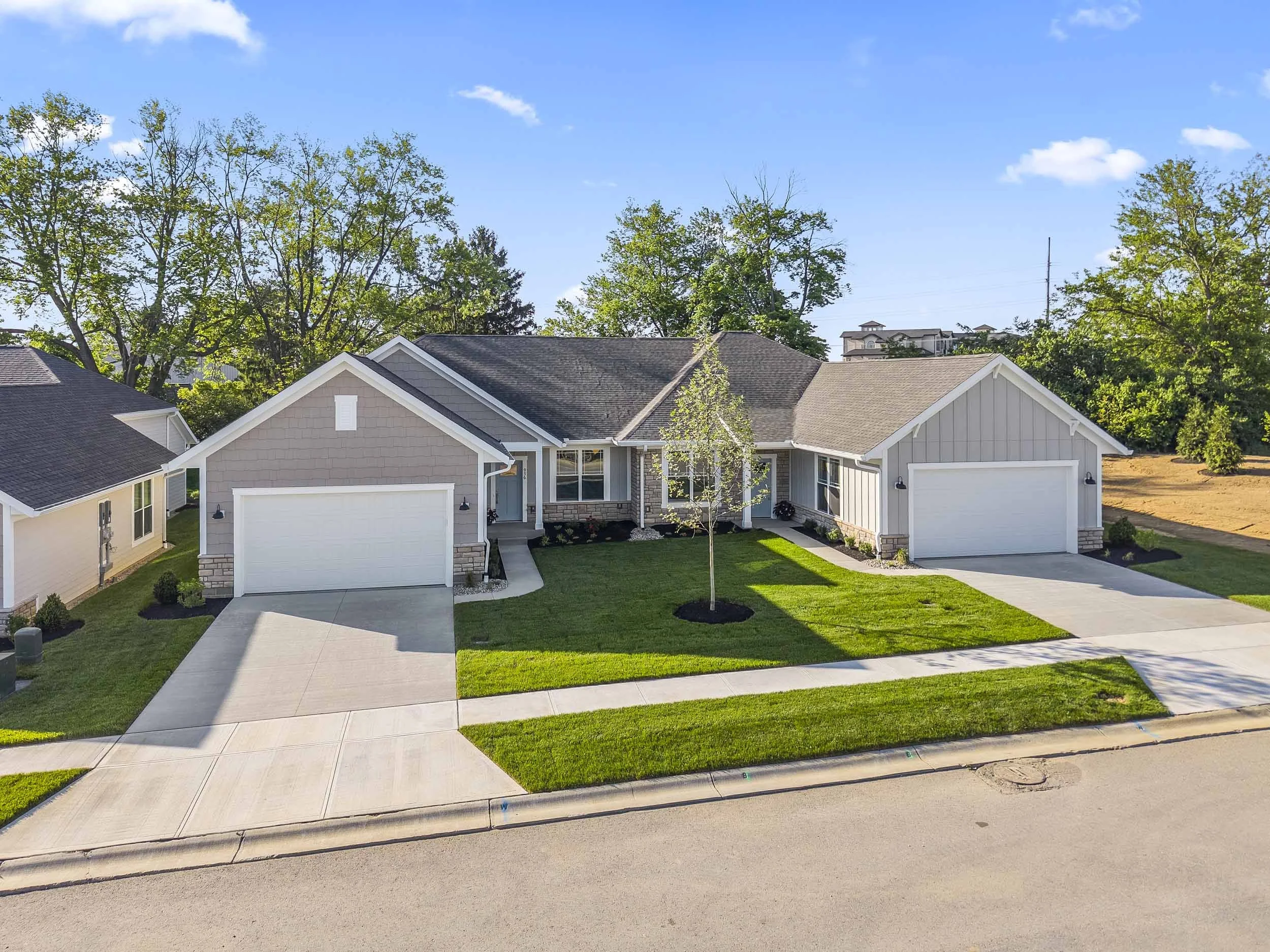A suburban house with a front lawn, driveway, and attached garage. Trees and a blue sky with clouds are visible in the background.